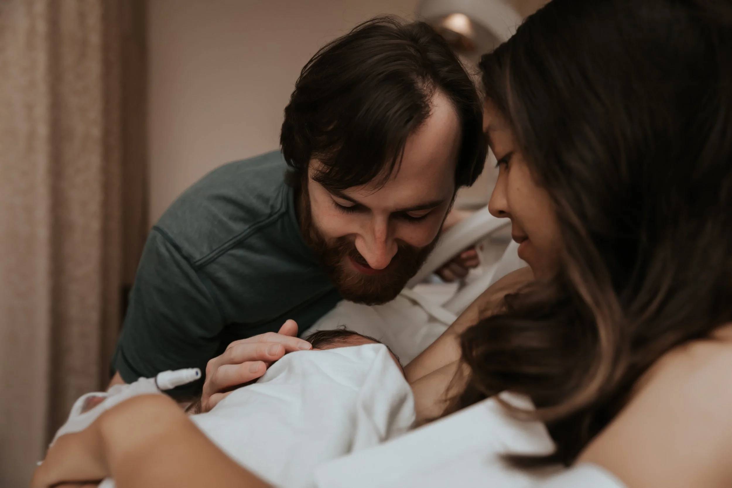 Photo of mom and dad gazing at newborn baby. Photo taken by Bay Area Birth Photographer Paige Driscoll. 