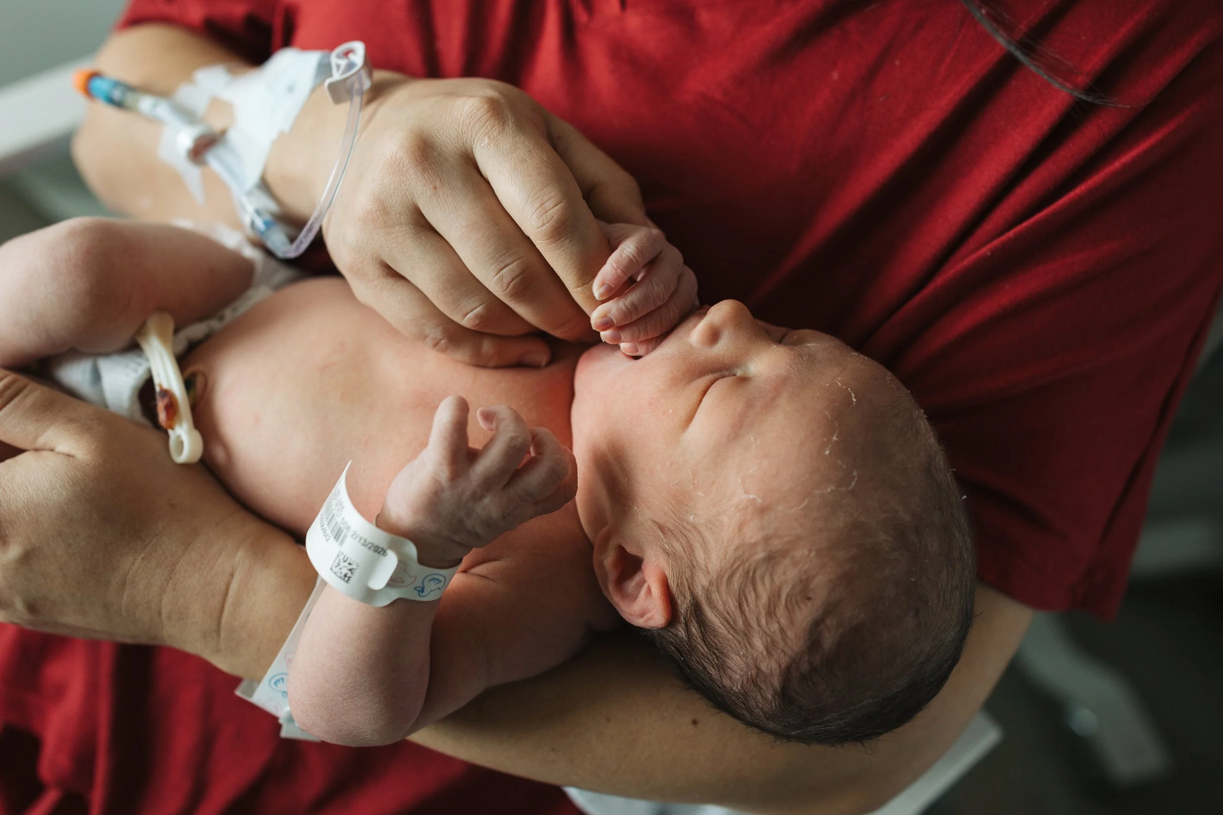 Newborn baby lying in their mother's arms in the hospital.