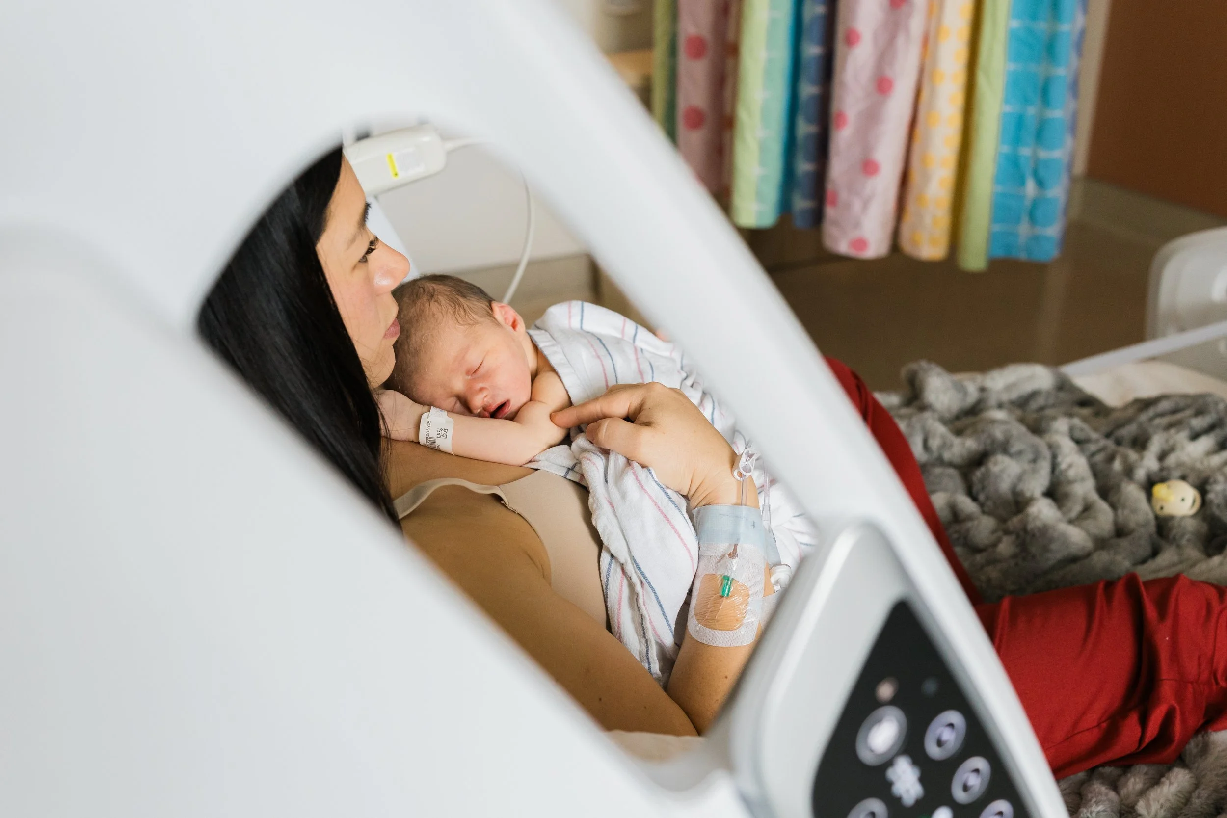 Newborn baby wrapped in a striped blanket lying in a hospital bassinet.