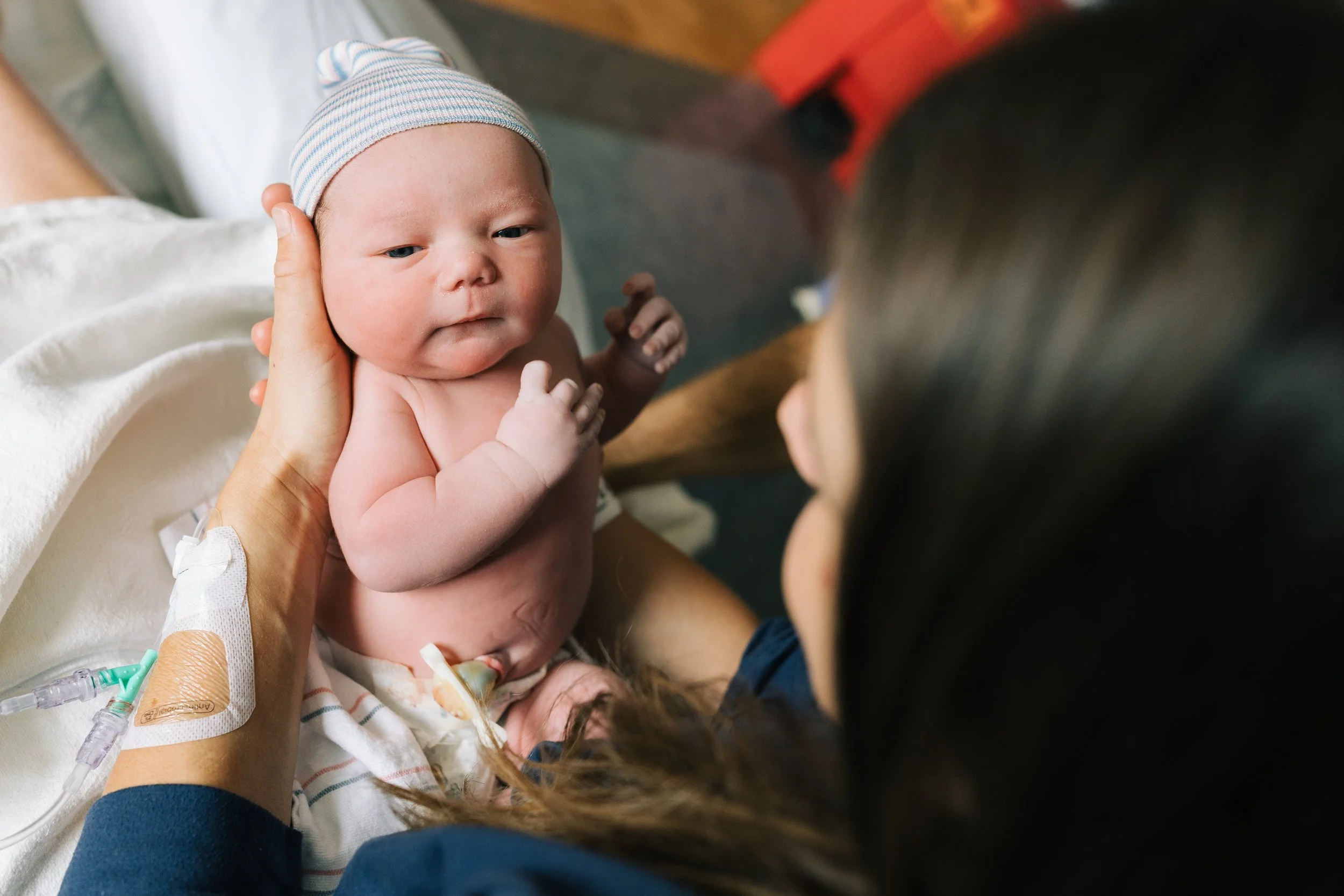 A chubby white baby being held by his mom in the hospital bed