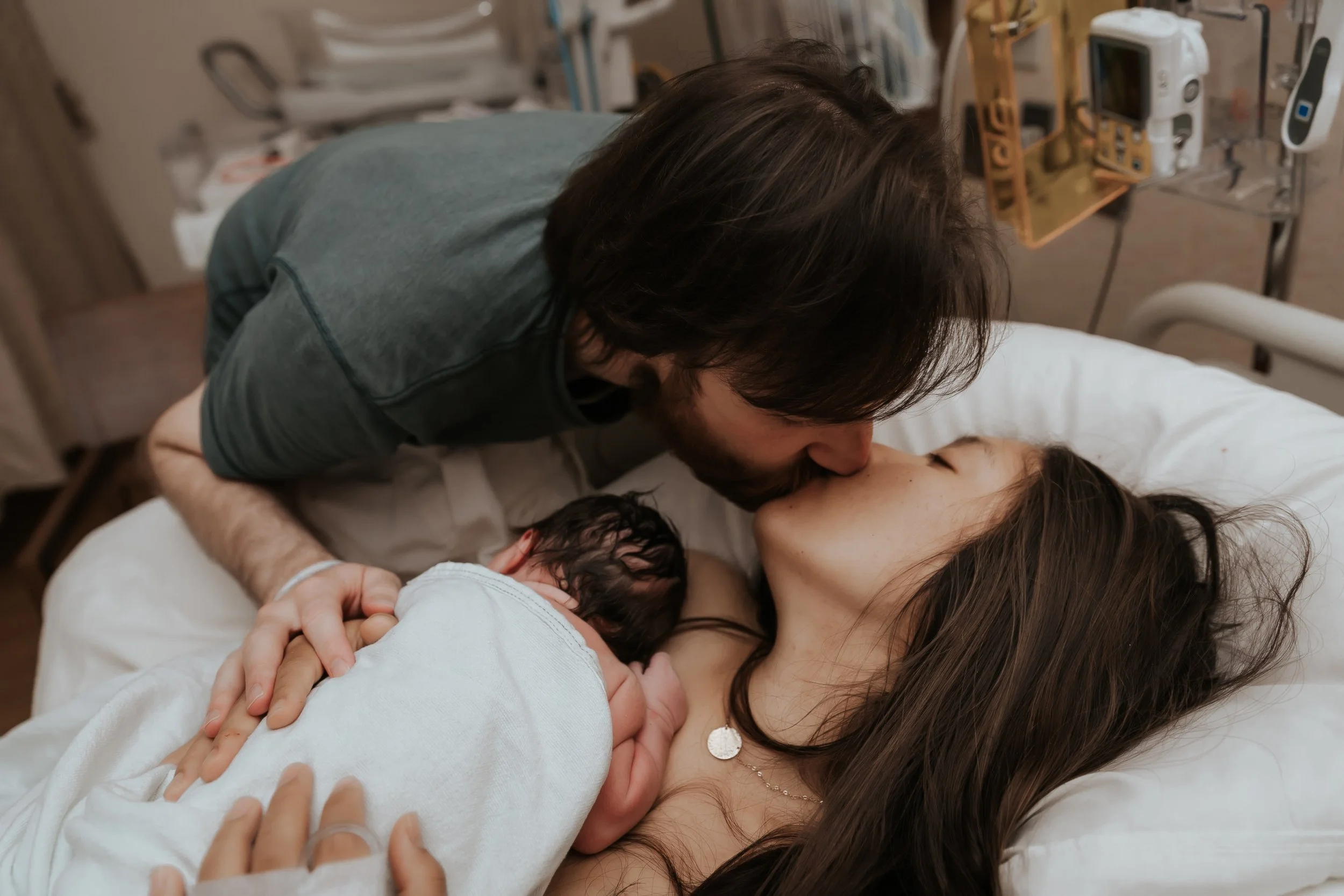 Mom and dad kissing while holding newborn baby.