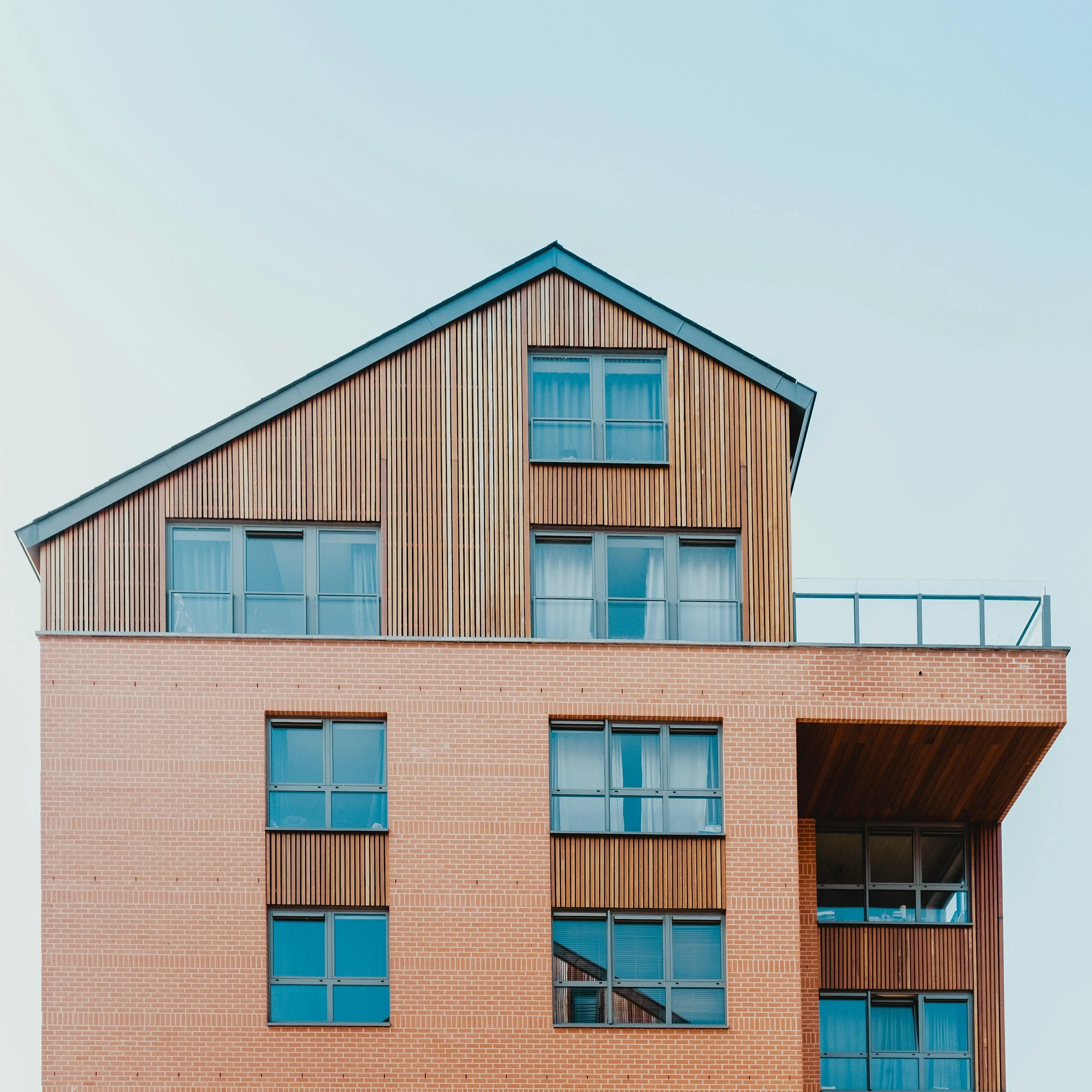 Modern multi-story building with brick and wooden exterior and large windows.