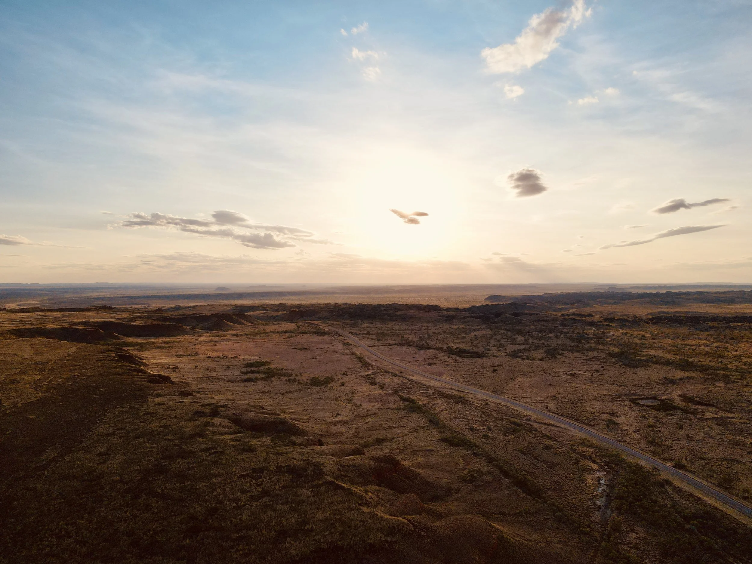 Aerial view of a desert landscape with a dirt road, under a sky with scattered clouds at sunset.