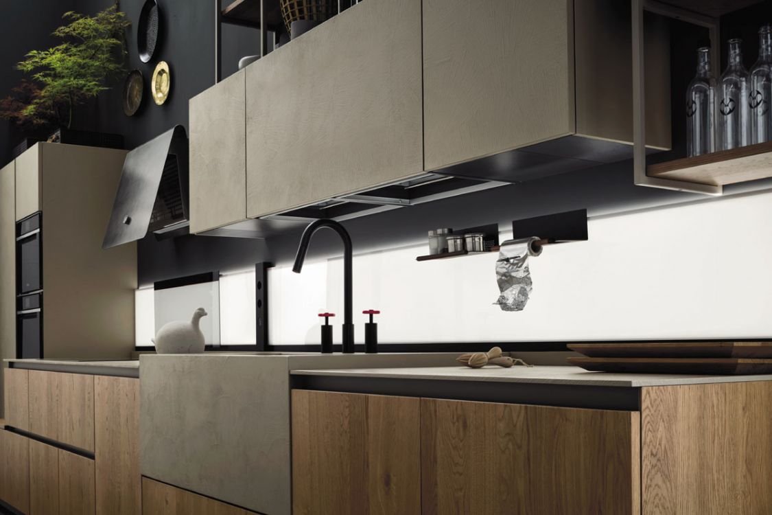Modern kitchen with light wood cabinets, black faucet, and a white swan figurine on the counter. There are upper cabinets, glass bottles, and a shelf with small jars, with a window behind the counter.