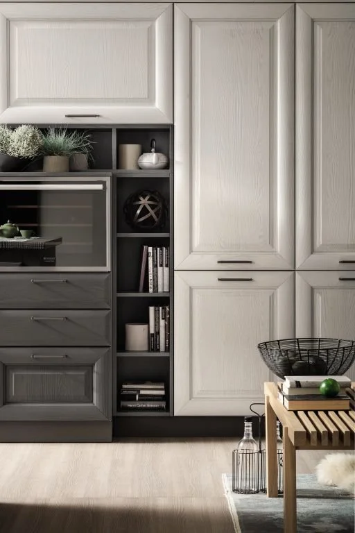 Kitchen with white cabinets and gray open shelves, small plants, books, decorative objects, and a wooden table with a wire basket, a glass bottle, and a green apple.