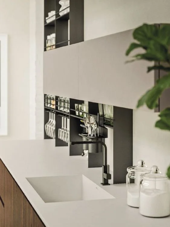 Modern kitchen with white countertop, black open shelving, hanging utensils, and a black faucet over a sink.