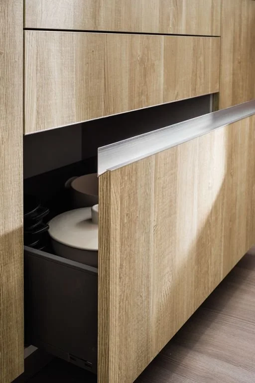 A wooden cabinet with an open drawer revealing kitchenware inside.