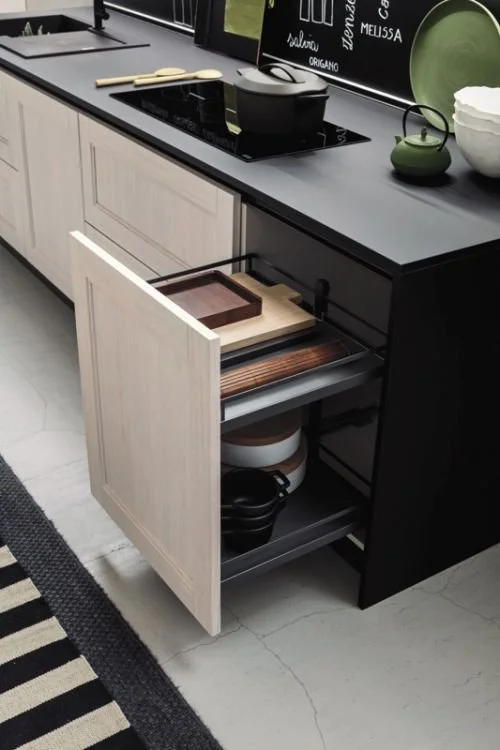 Open kitchen cabinet drawer revealing storage for cutting boards, bowls, and pots in a modern kitchen.
