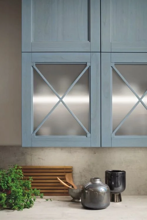 Close-up of a kitchen with gray cabinets and metallic accents, decorative vases, and a wooden tray on the countertop.
