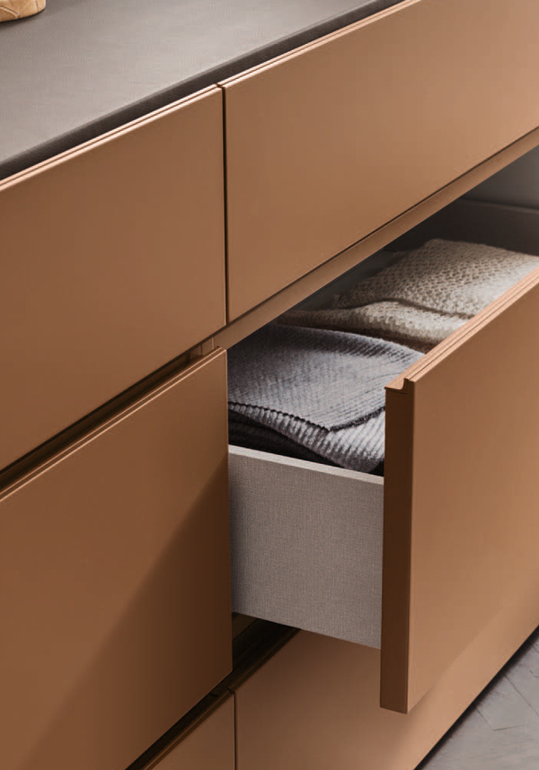 An open drawer in a beige dresser shows folded towels and fabric inside.