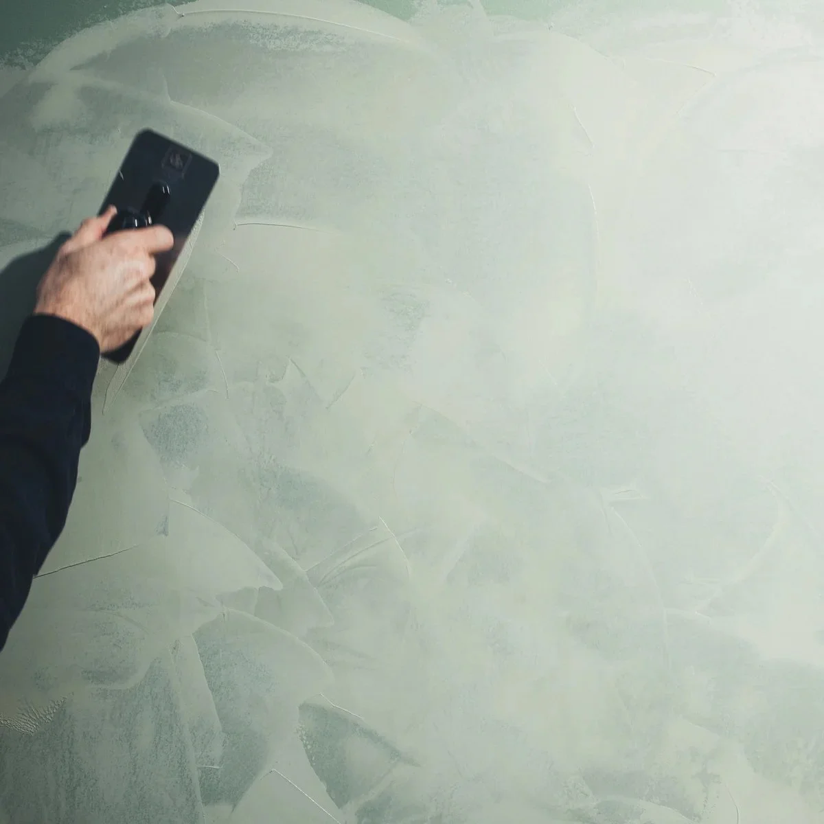 Person holding a smartphone taking a photo of a light-colored textured wall.