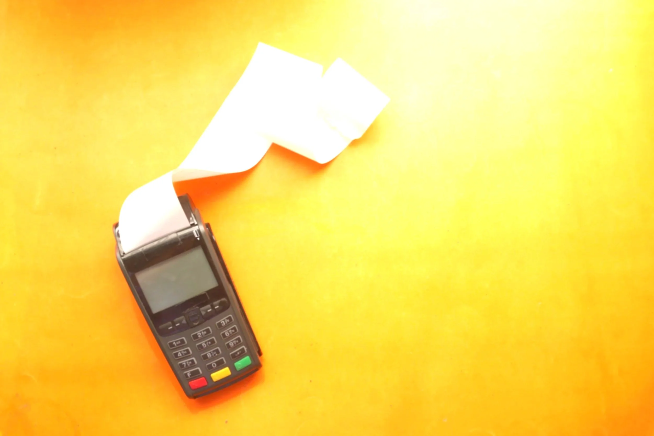 A point-of-sale terminal with a receipt roll coming out, placed on an orange surface.