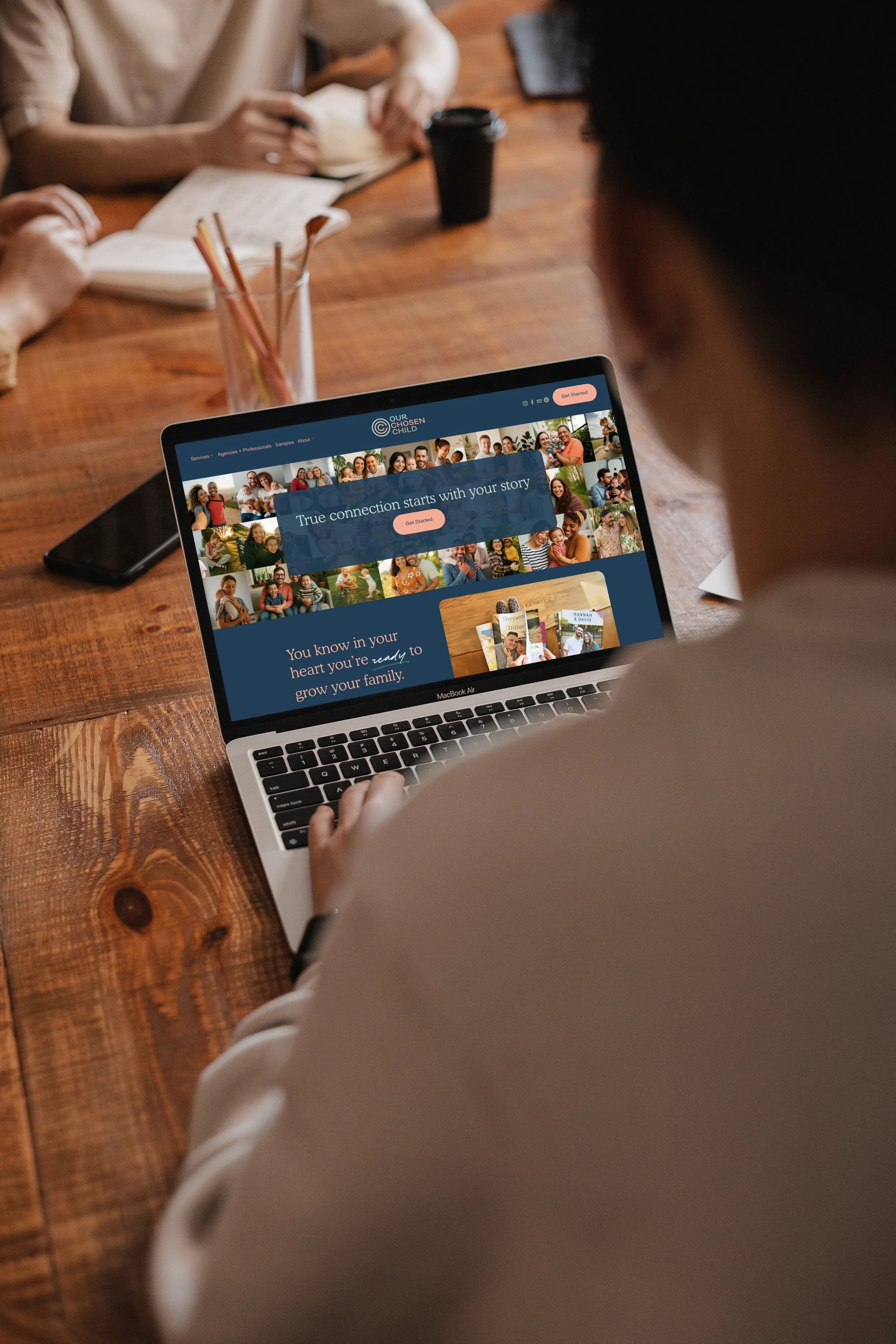 Person using a MacBook Air to browse the 'Our Chosen Child' website. The website displays children's photos and a message about family growth.