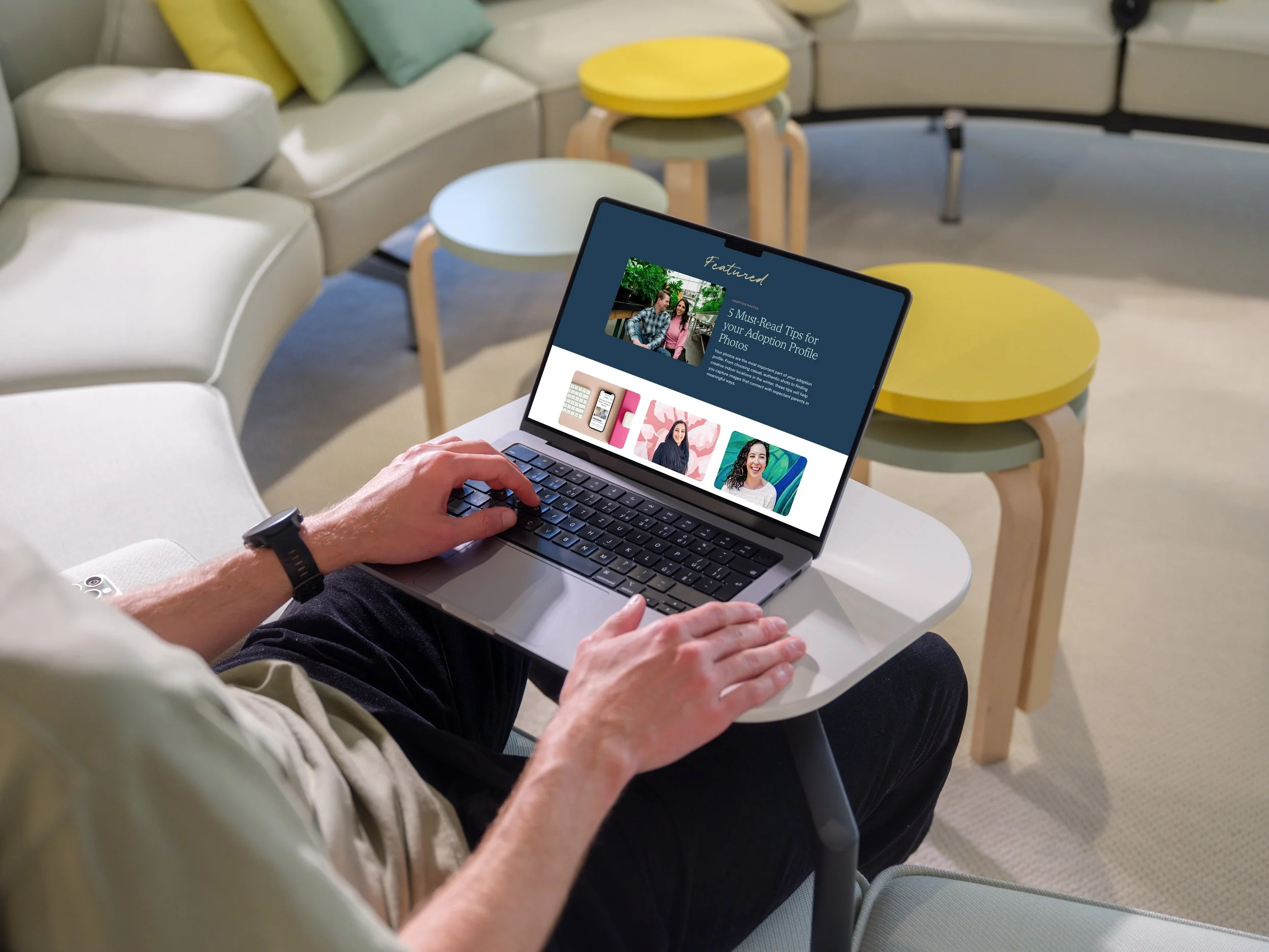 Person using a laptop in a bright, modern lounge area with colorful round tables and white seating.