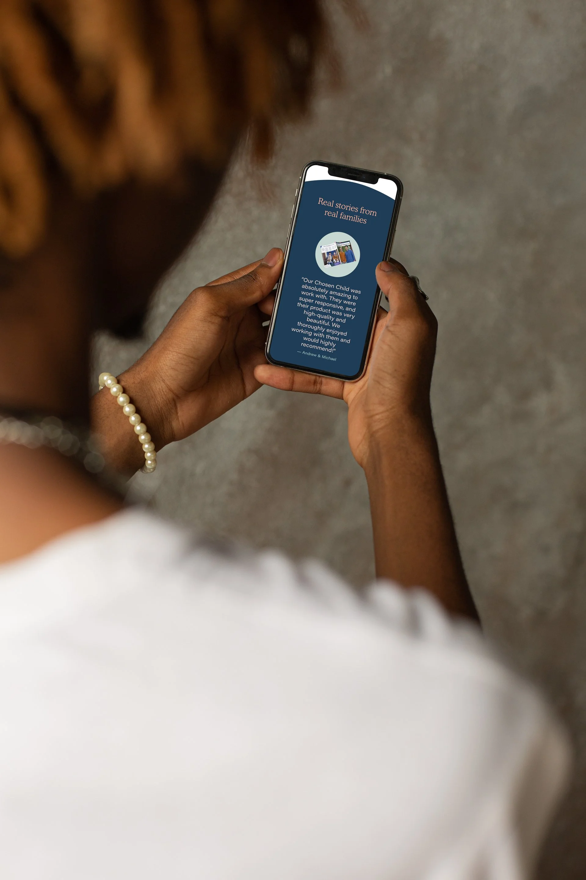 A person holding a smartphone displaying a story about a child's foster experience, with a background of a concrete wall.