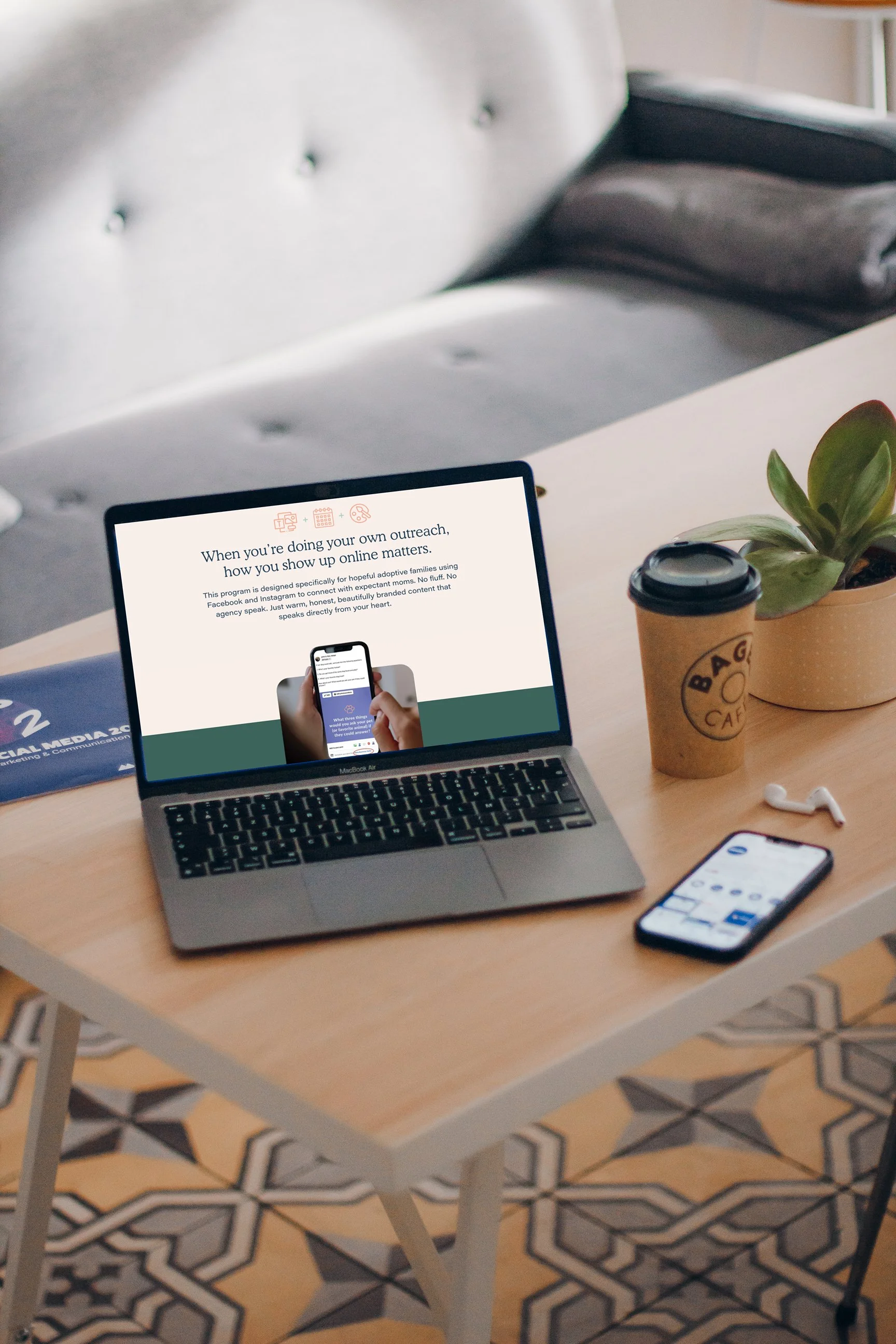 A tablet displaying an outreach program, a smartphone, a coffee cup, and a small potted plant on a wooden table with patterned tile flooring.