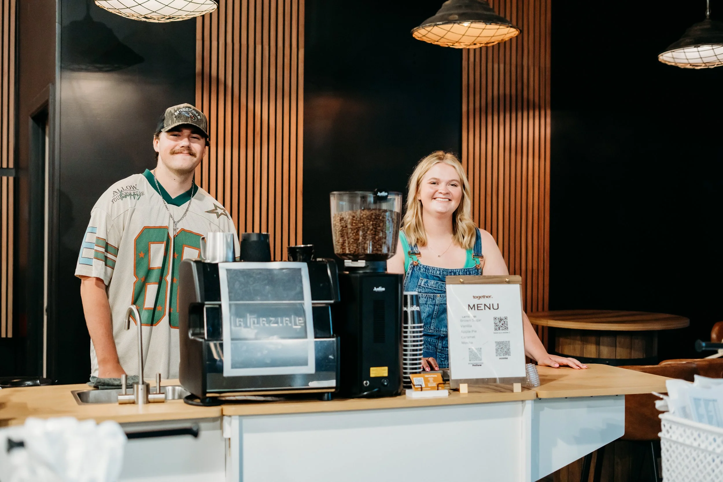 Close-up of a coffee counter with a large sign reading 'together. coffee co' in black text, and a partially visible person behind it preparing coffee with espresso machines.