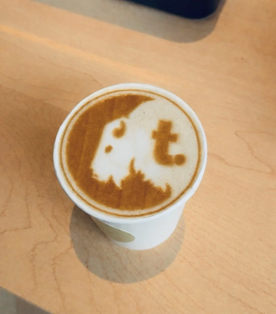 Close-up of a coffee counter with a large sign reading 'together. coffee co' in black text, and a partially visible person behind it preparing coffee with espresso machines.