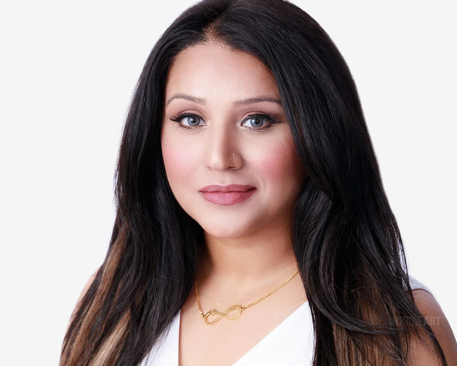 A woman with long black hair streaked with brown, blue eyes, light makeup, and a gold necklace with an infinity symbol.