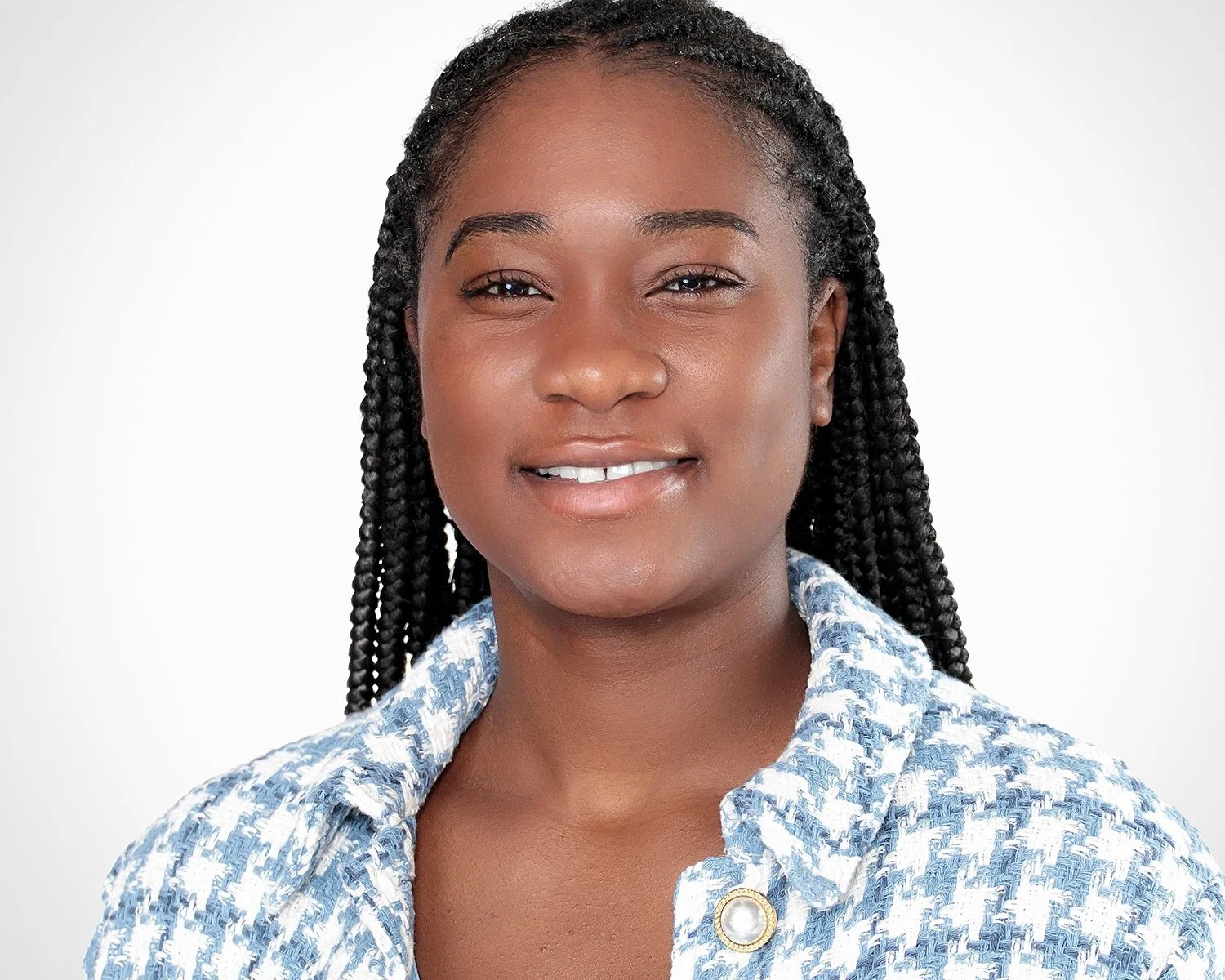 A portrait of a smiling African American woman with braided hair wearing a patterned blue and white jacket with a pearl button.