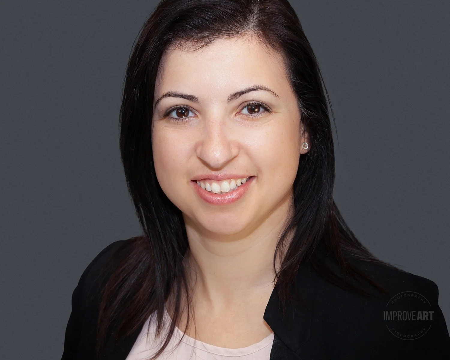 A professional woman with shoulder-length dark hair smiling at the camera against a gray background.