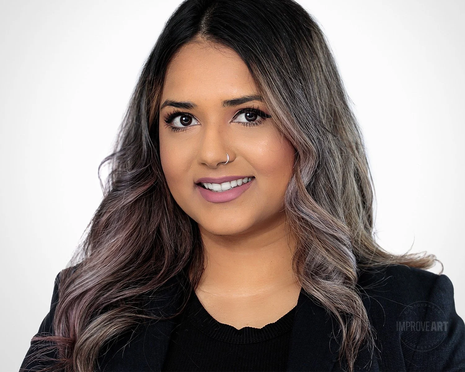 Headshot of a woman with long, wavy hair, wearing a black blazer, smiling against a white background.