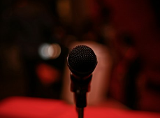 Close-up of a microphone on a stand against a blurred red and dark background.