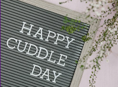 A letter board with the message "HAPPY CUDDLE DAY" surrounded by pink blossoming branches.