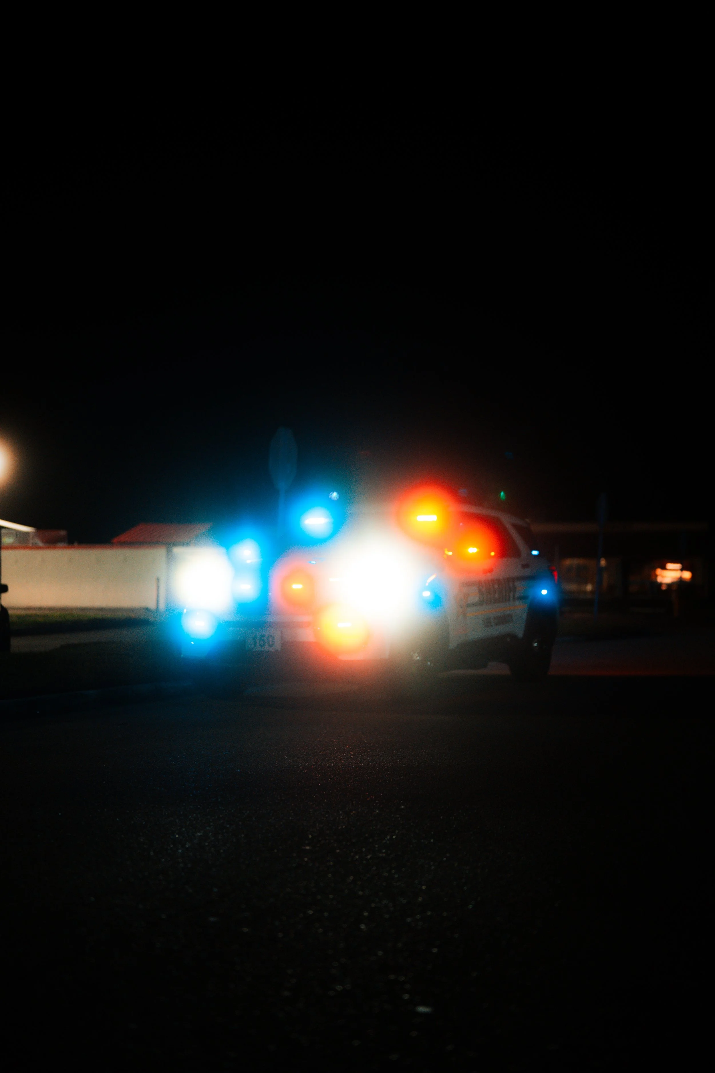 A police car with flashing red, blue, and white lights at night.