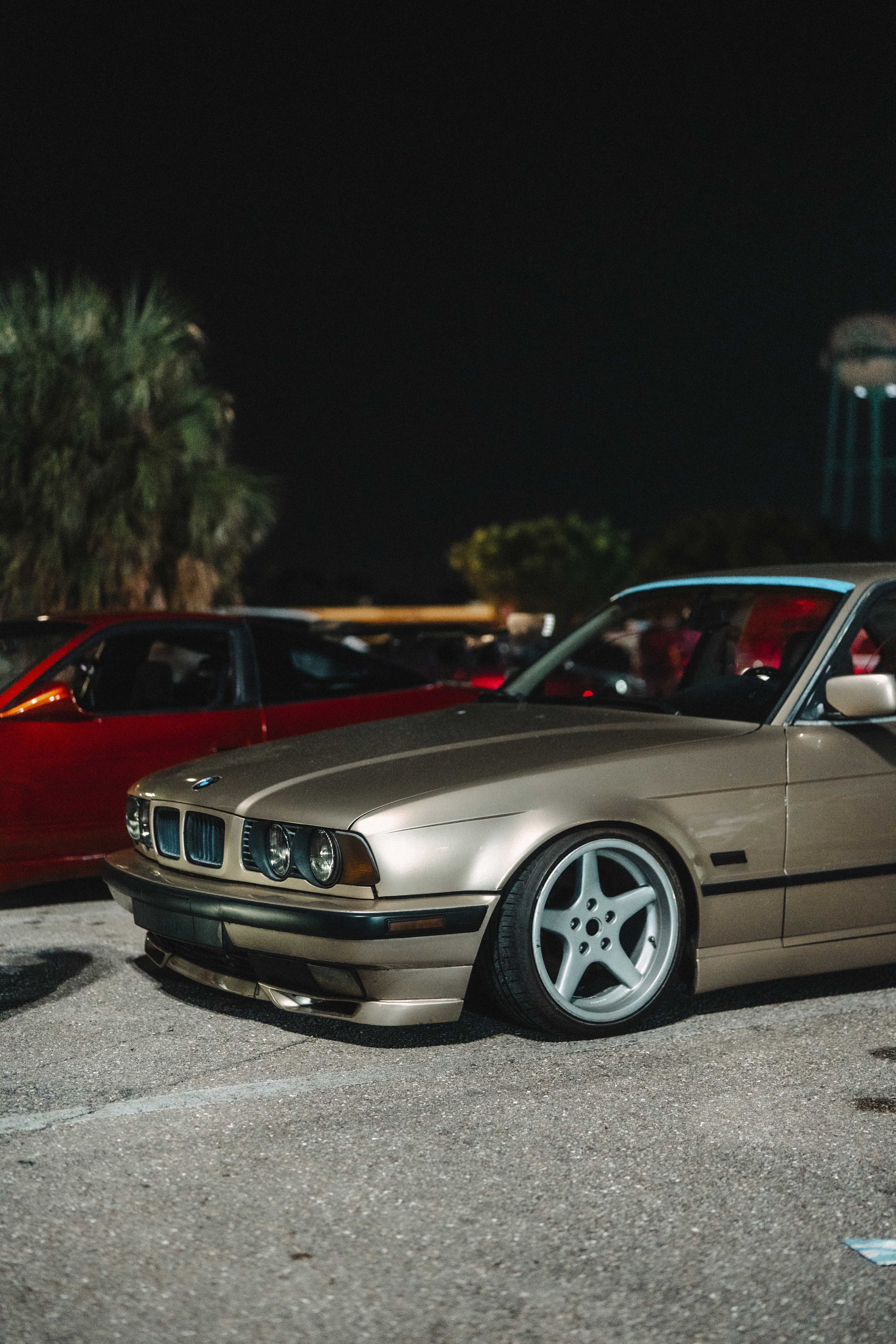 A classic BMW coupe parked on a street at night, with other cars and trees in the background.