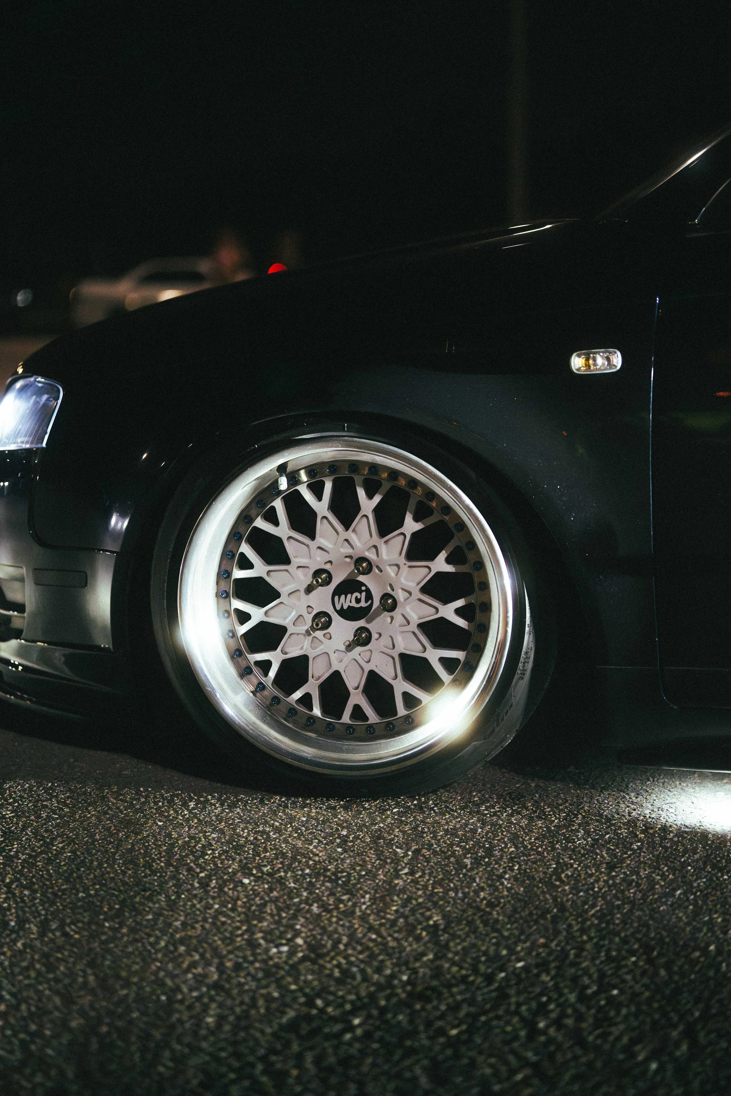 Close-up of car wheel with a custom multi-spoke rim at night on a paved surface.