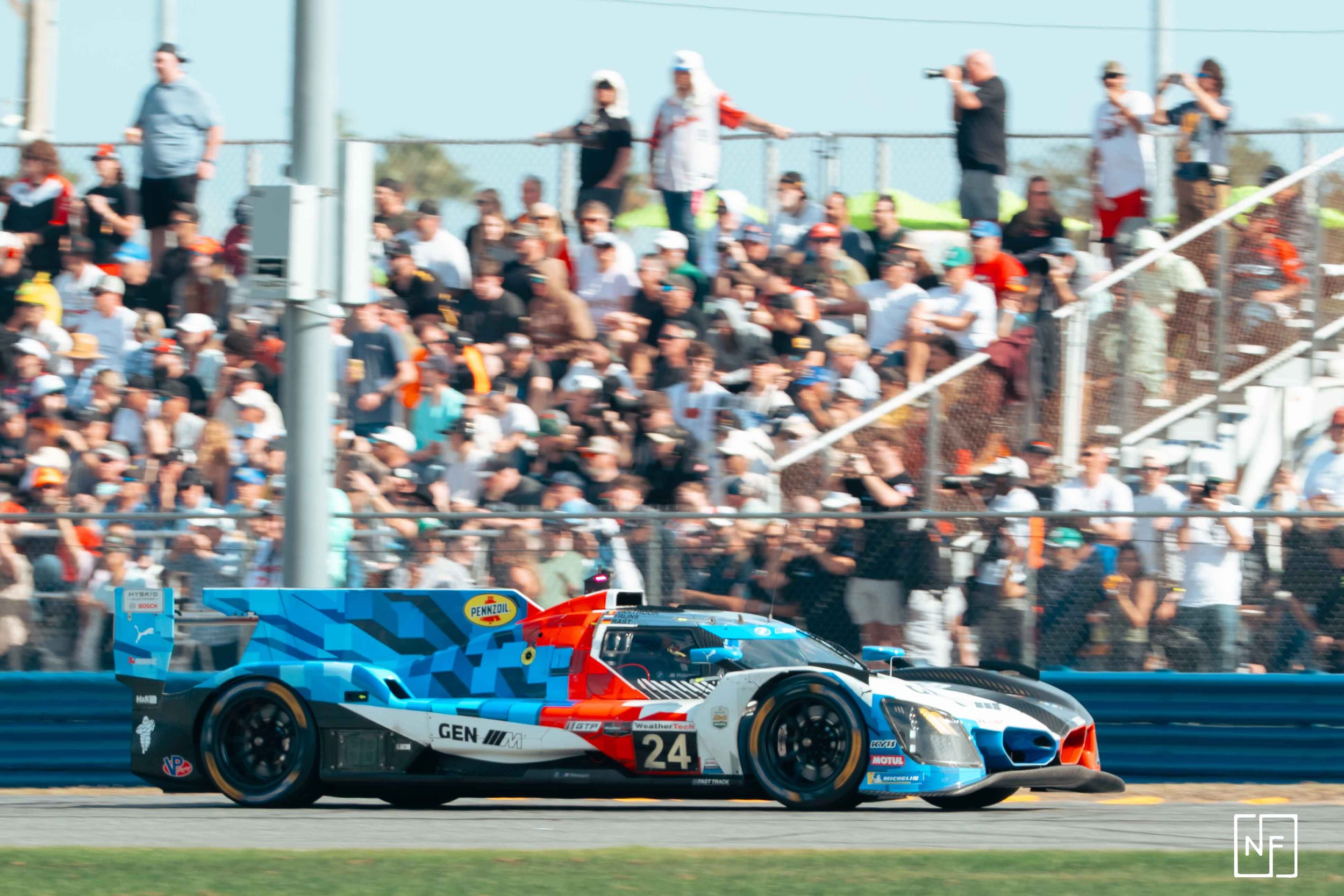 A race car on a race track with a large crowd in the bleachers in the background