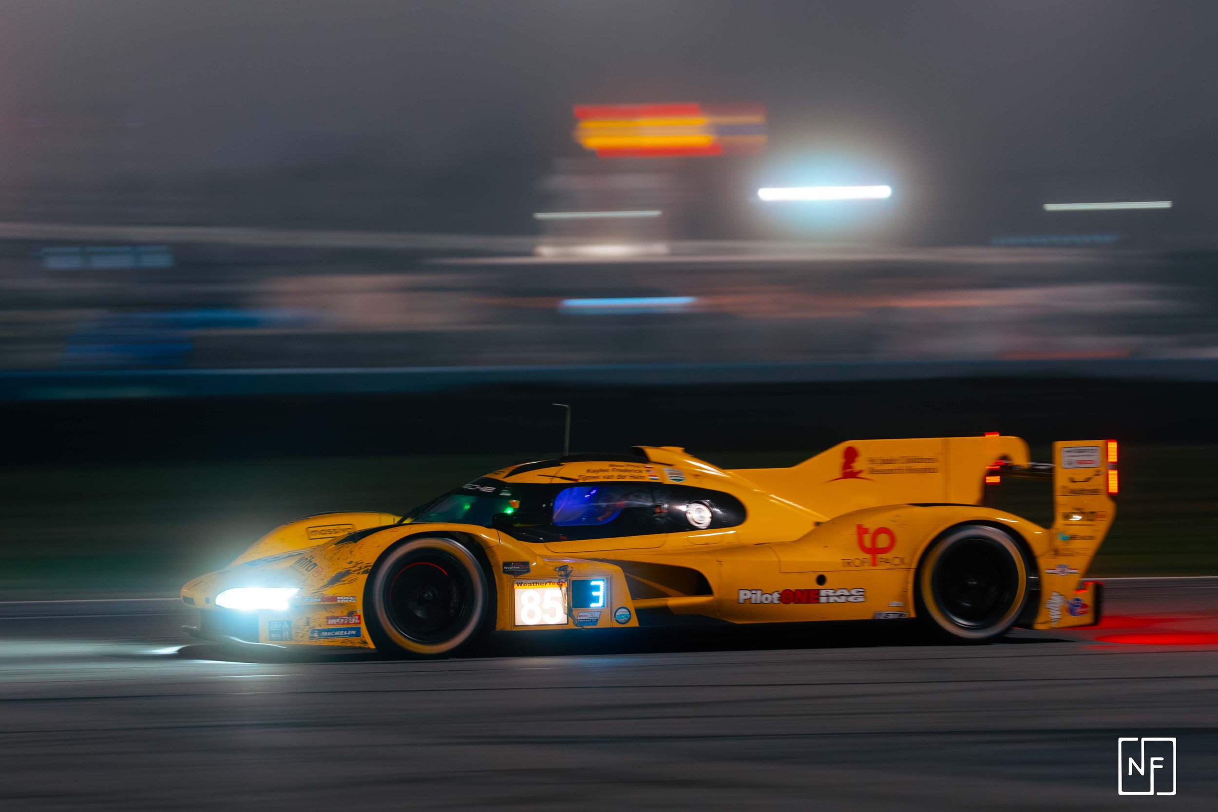 A yellow race car speeding on a track at night, with headlights on and motion blur indicating high speed.