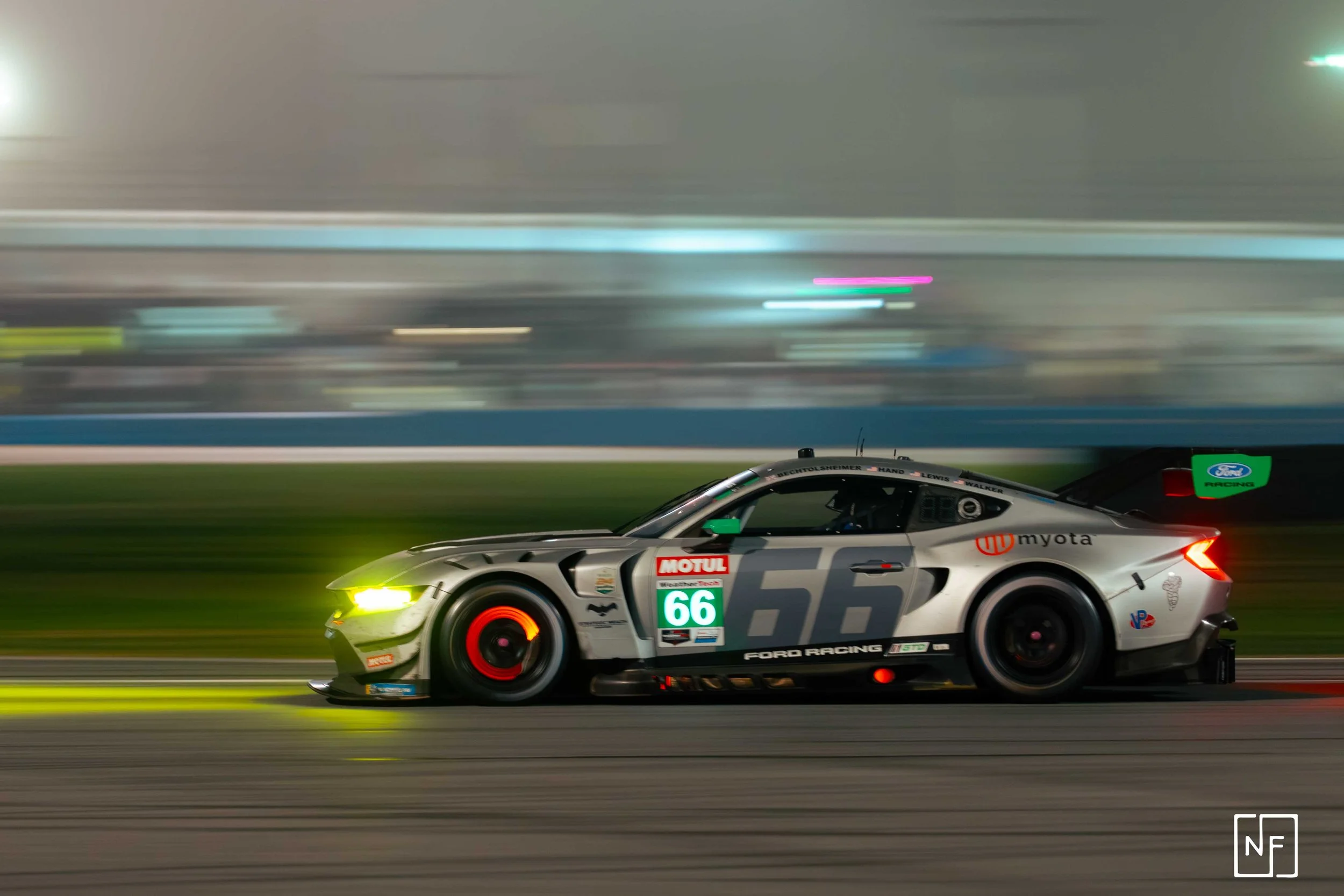 Race car moving fast on a track during night, with motion blur background and illuminated headlights.