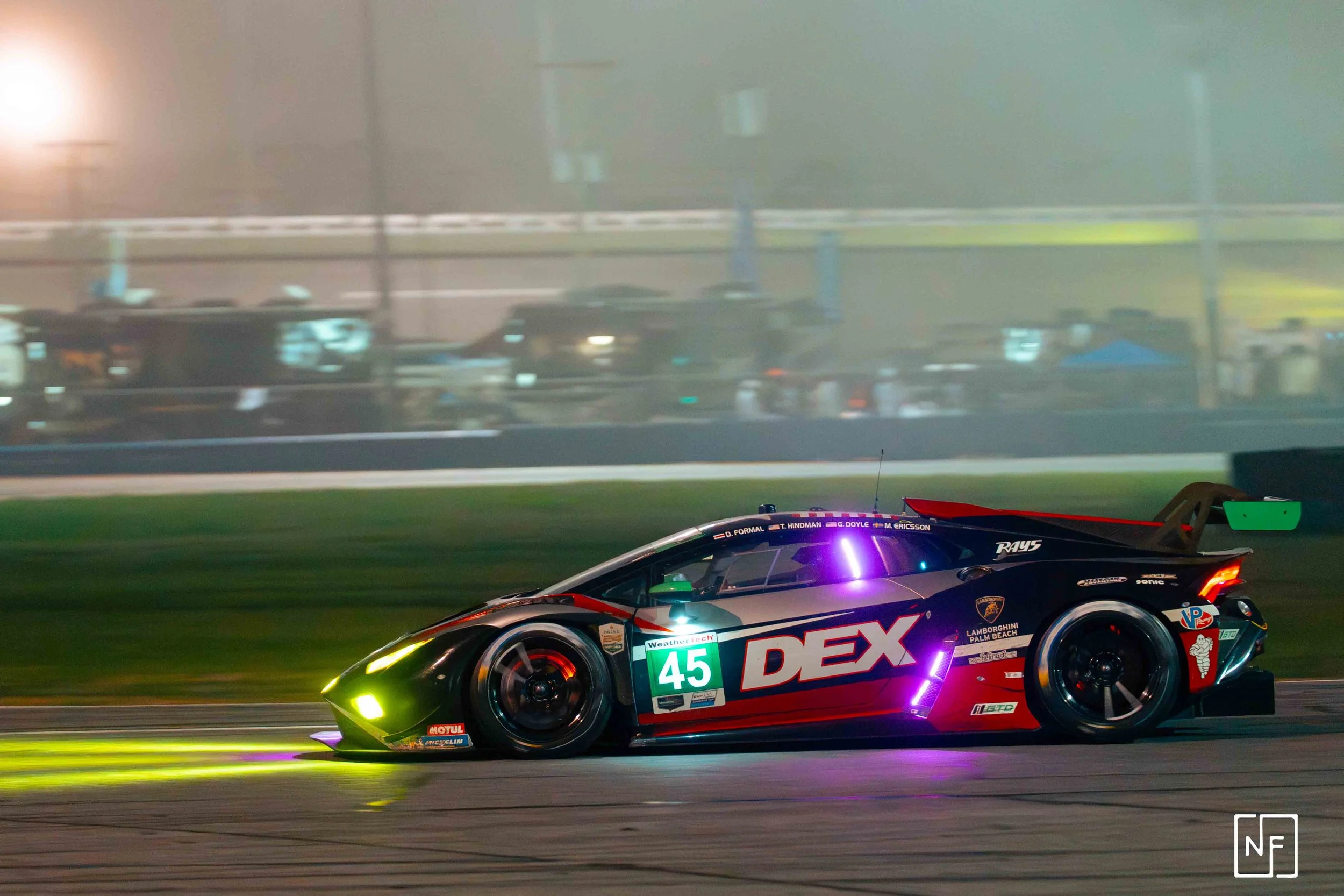 A race car with the number 45 and the DEX logo, driving on a race track at night, emitting colorful lights and smoke.