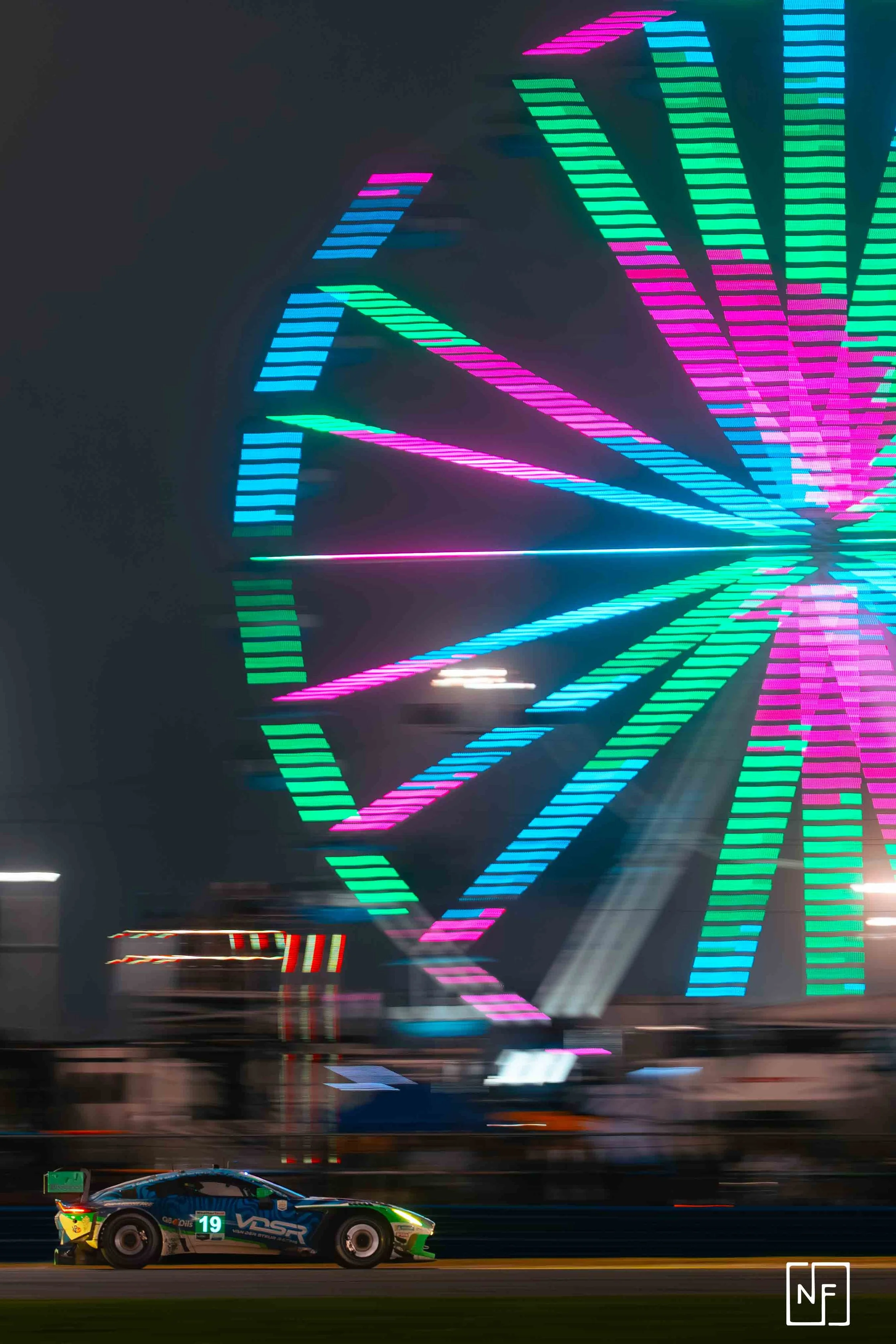 A race car on a track at night with a brightly lit Ferris wheel in the background.
