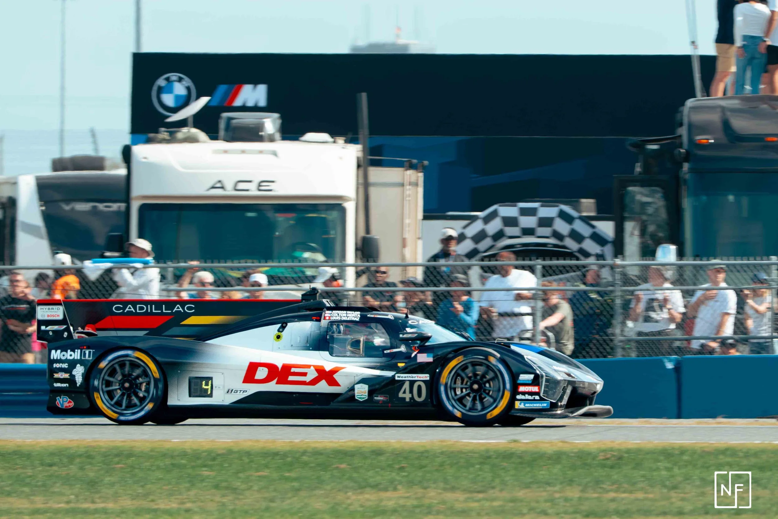 Race car with DEX sponsorship and number 40, on a racetrack with spectators and vehicles in the background.