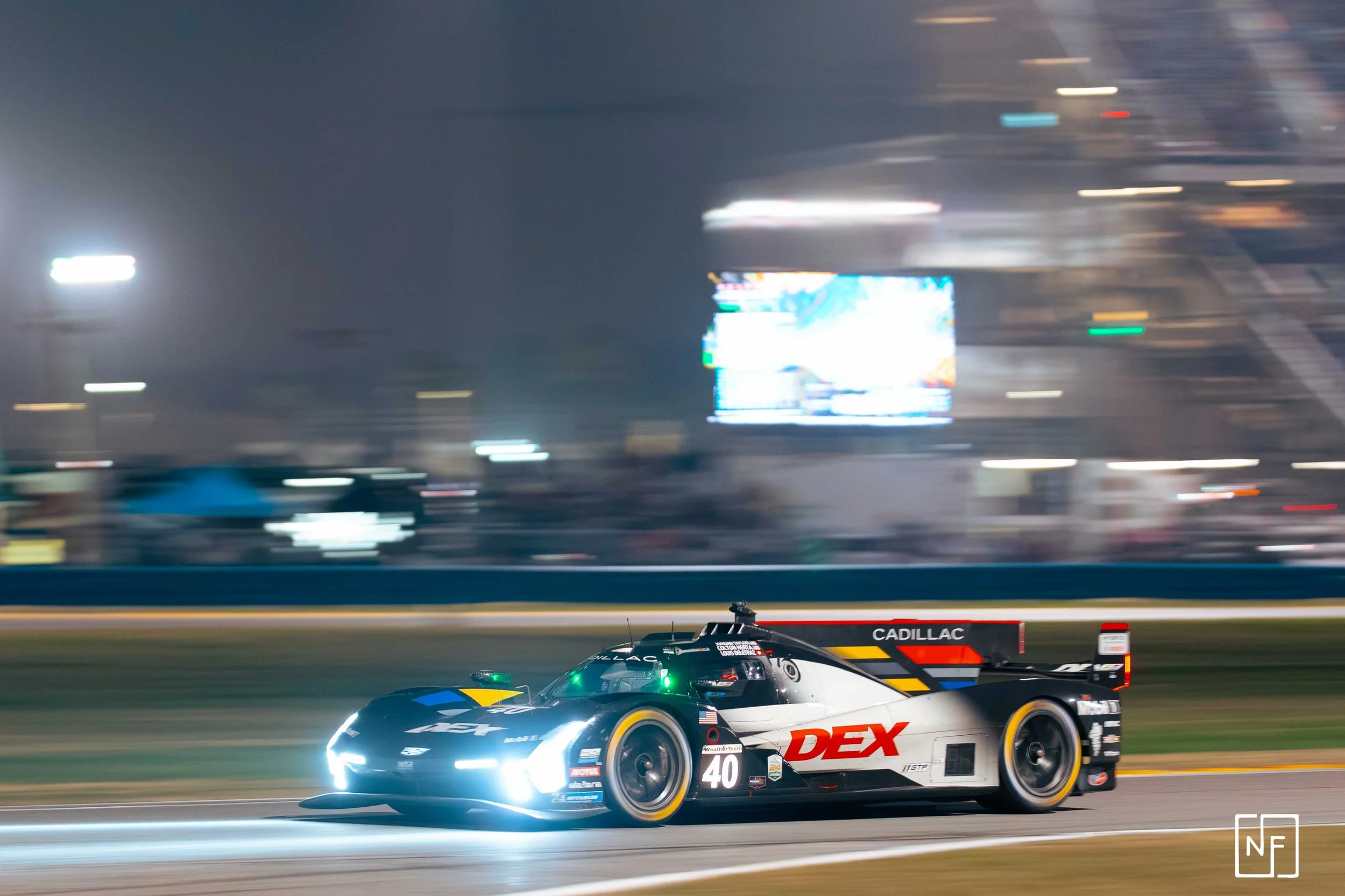 A racing car with the number 40 on it speeding on a race track at night, with bright headlights and blurred background.