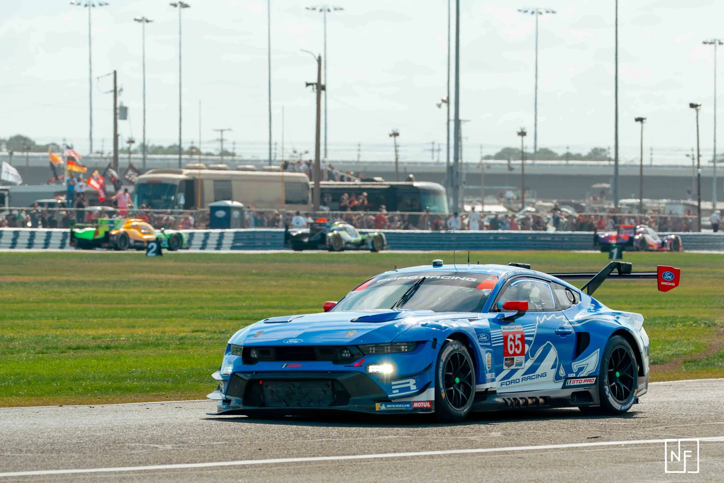 A blue racing car on a race track with other cars and a crowd in the background.