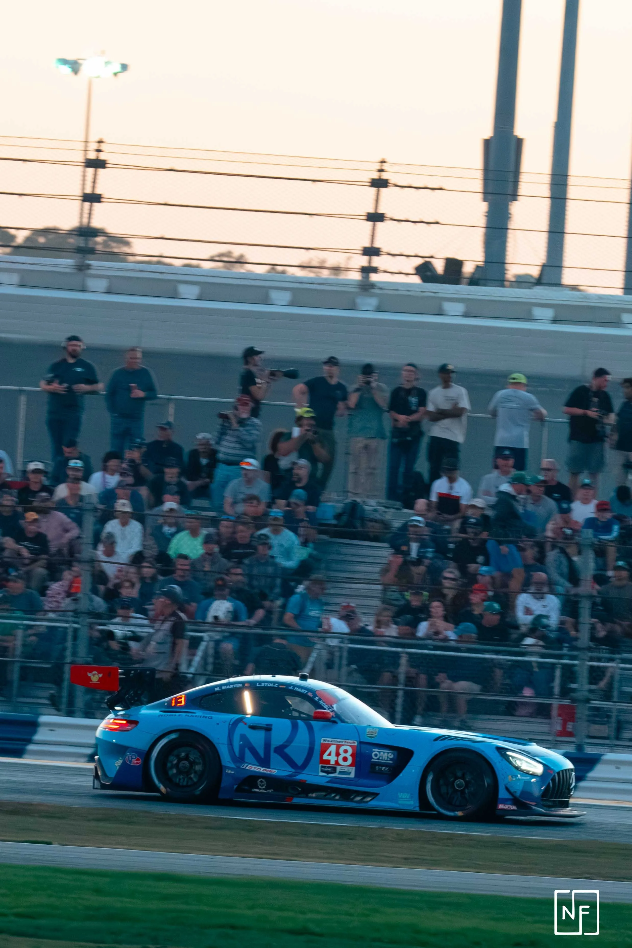 A blue race car on a racetrack with a crowd of spectators in the background.