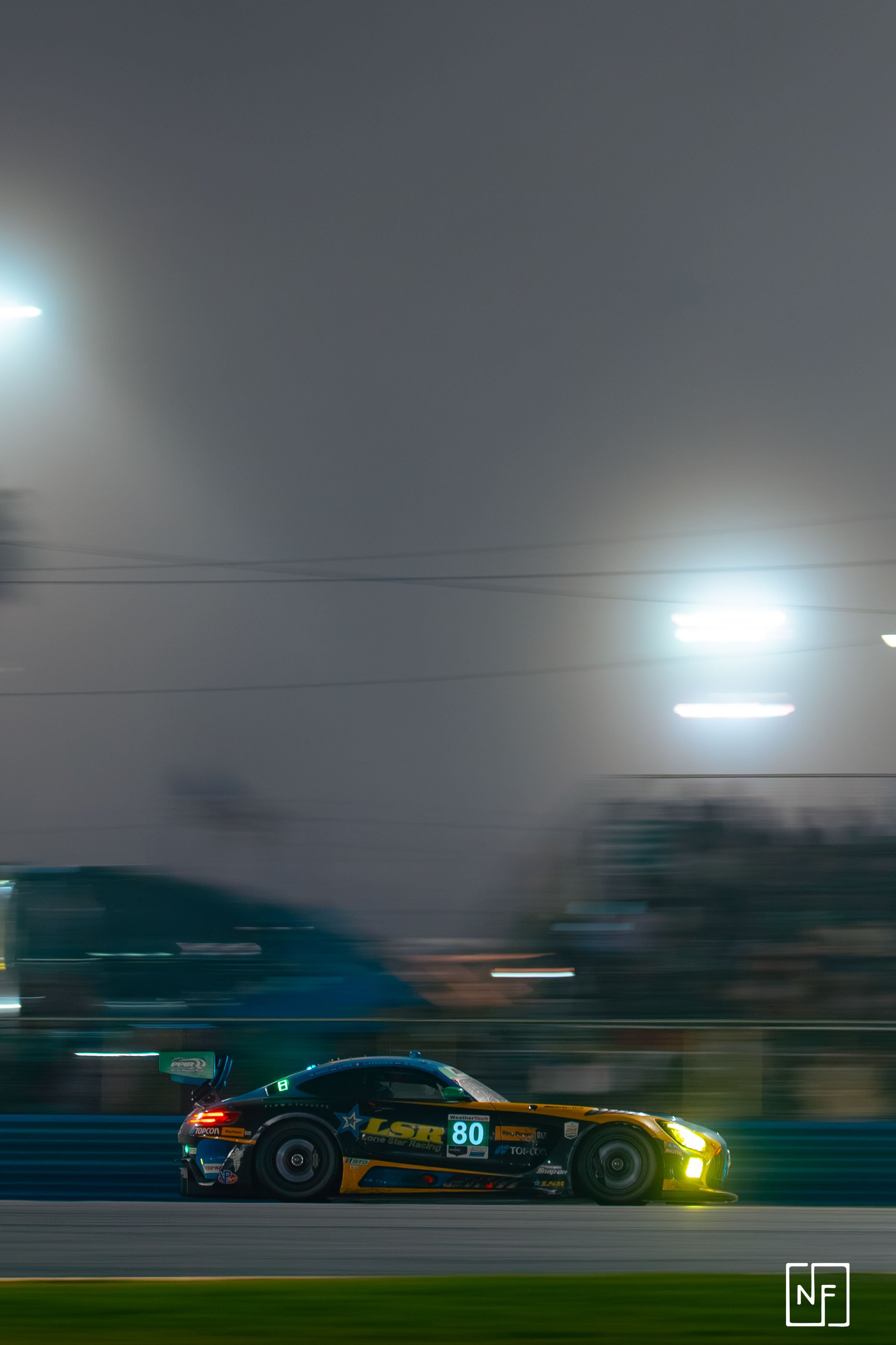 A race car speeding on a track at night, illuminated by bright lights, with blurred background.