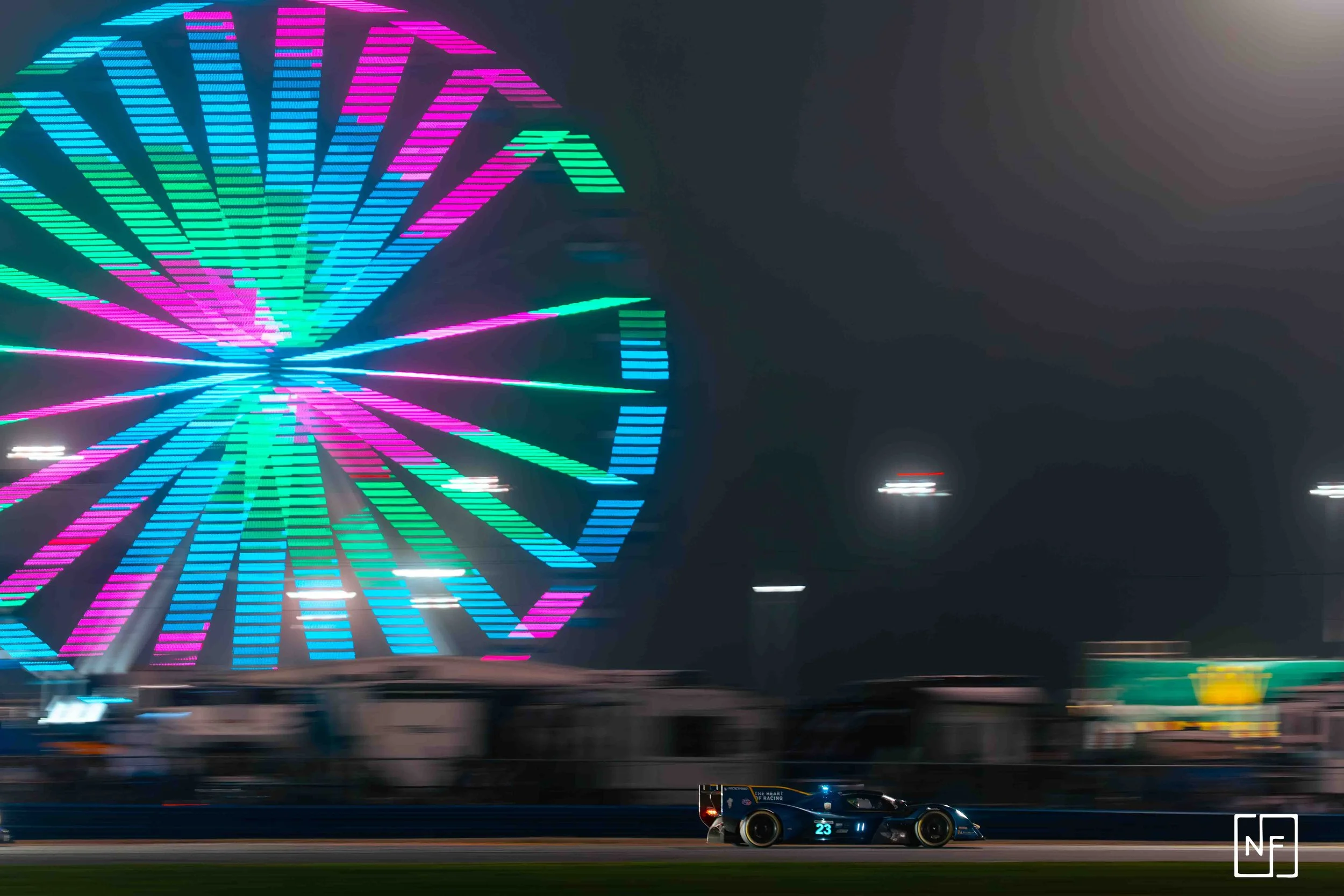 A racing car on a track at night with a large, colorful Ferris wheel illuminated in the background.