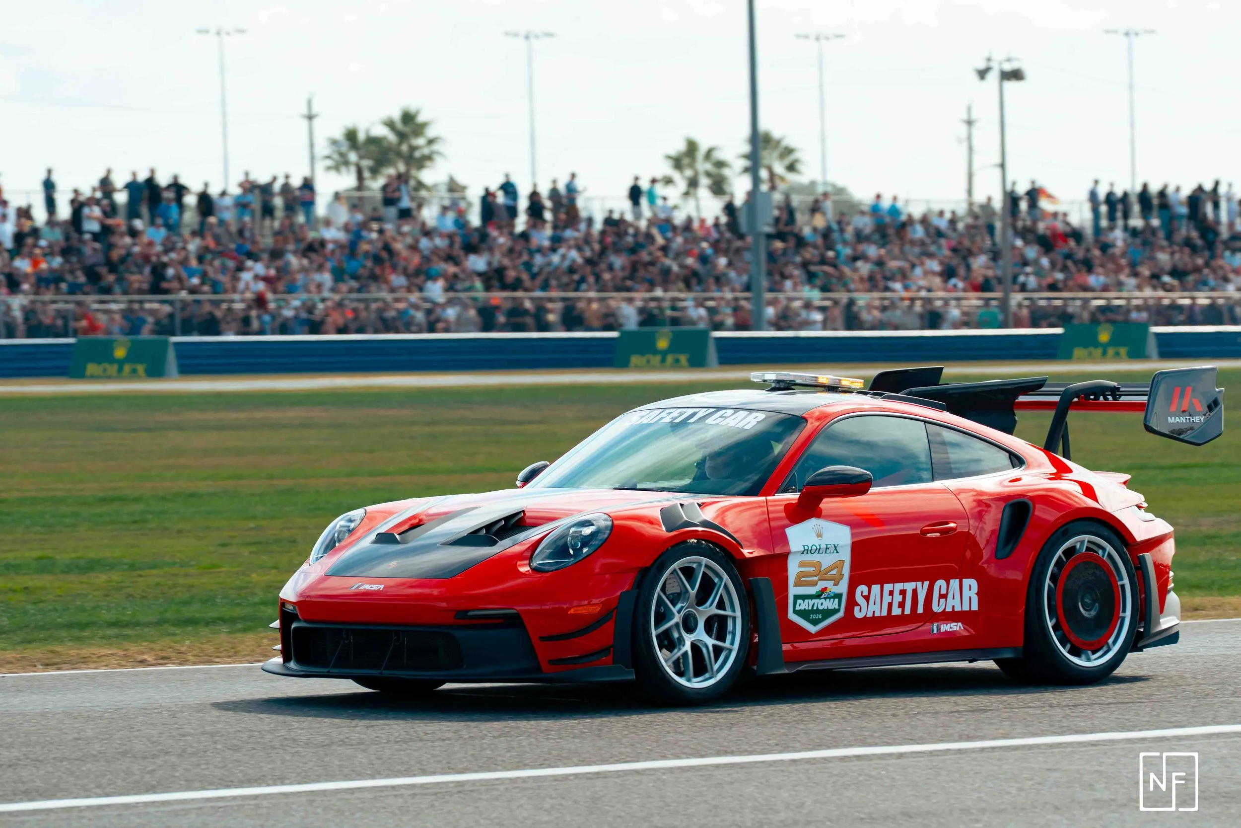 Red racing safety car on a race track with a crowd in the background.