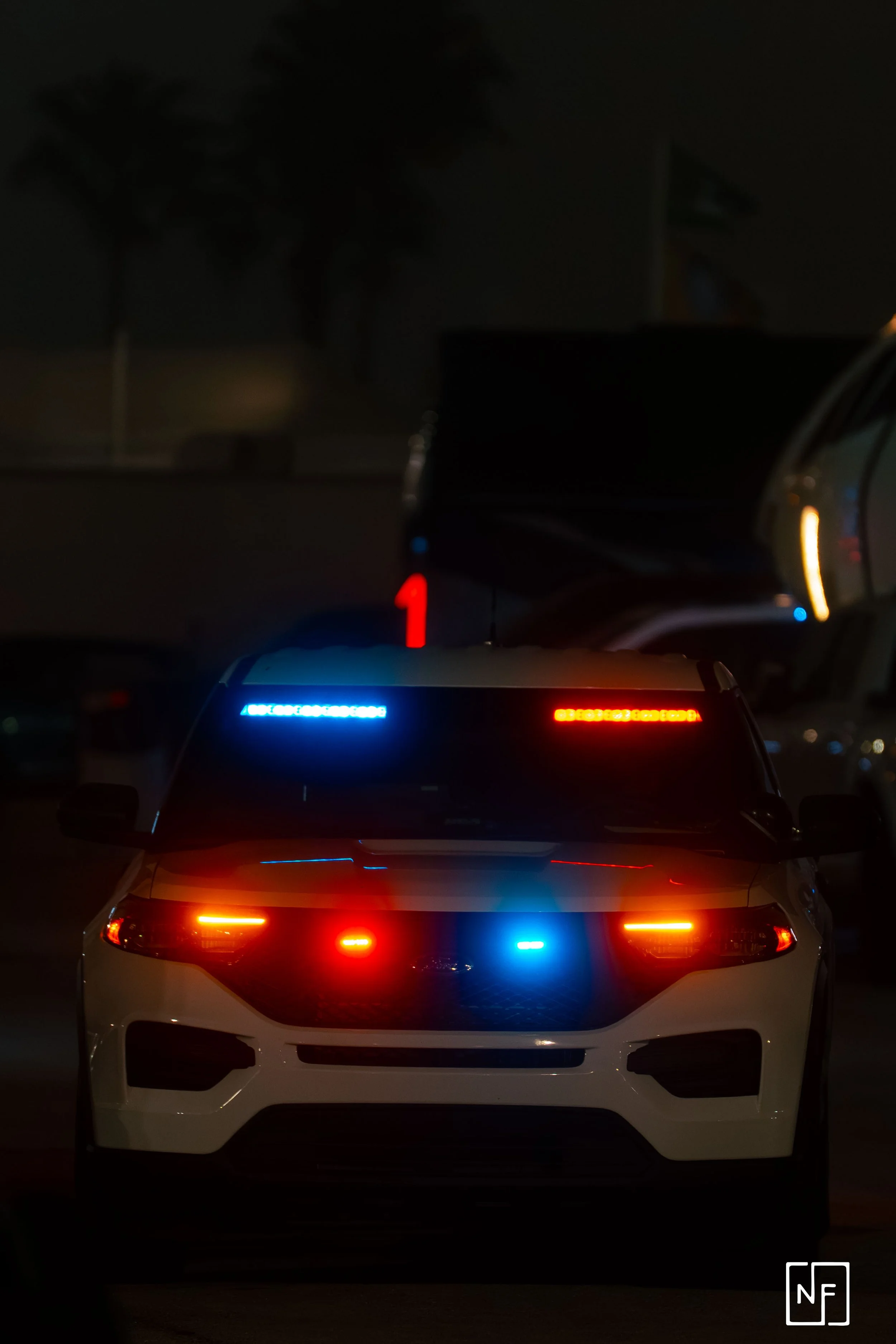 A police car with flashing red, blue, and amber lights at night.