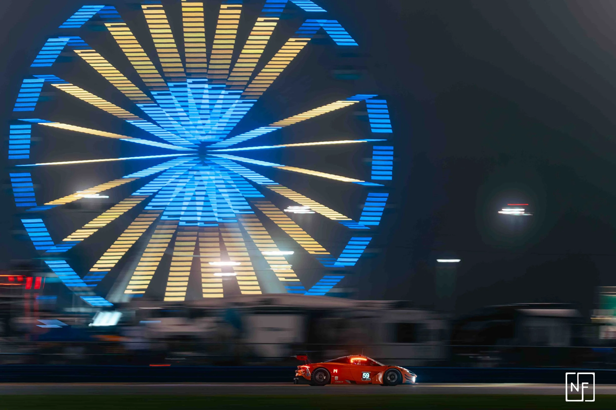 A red race car moving quickly on a track at night with a large illuminated Ferris wheel in the background.