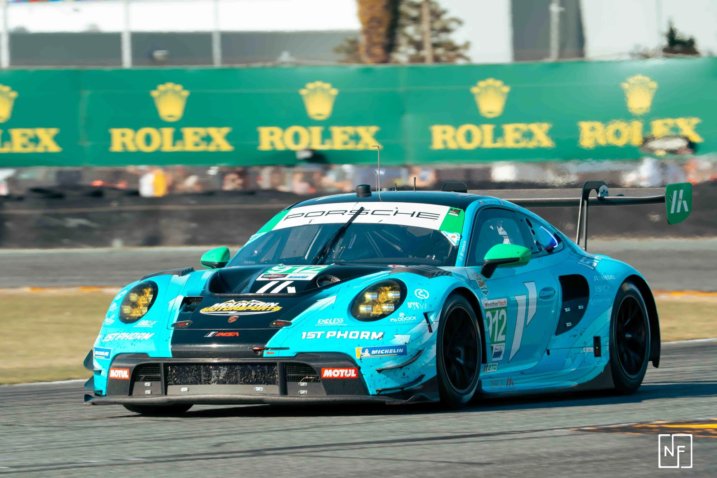 A blue Porsche race car on a racetrack with a green Rolex banner in the background.