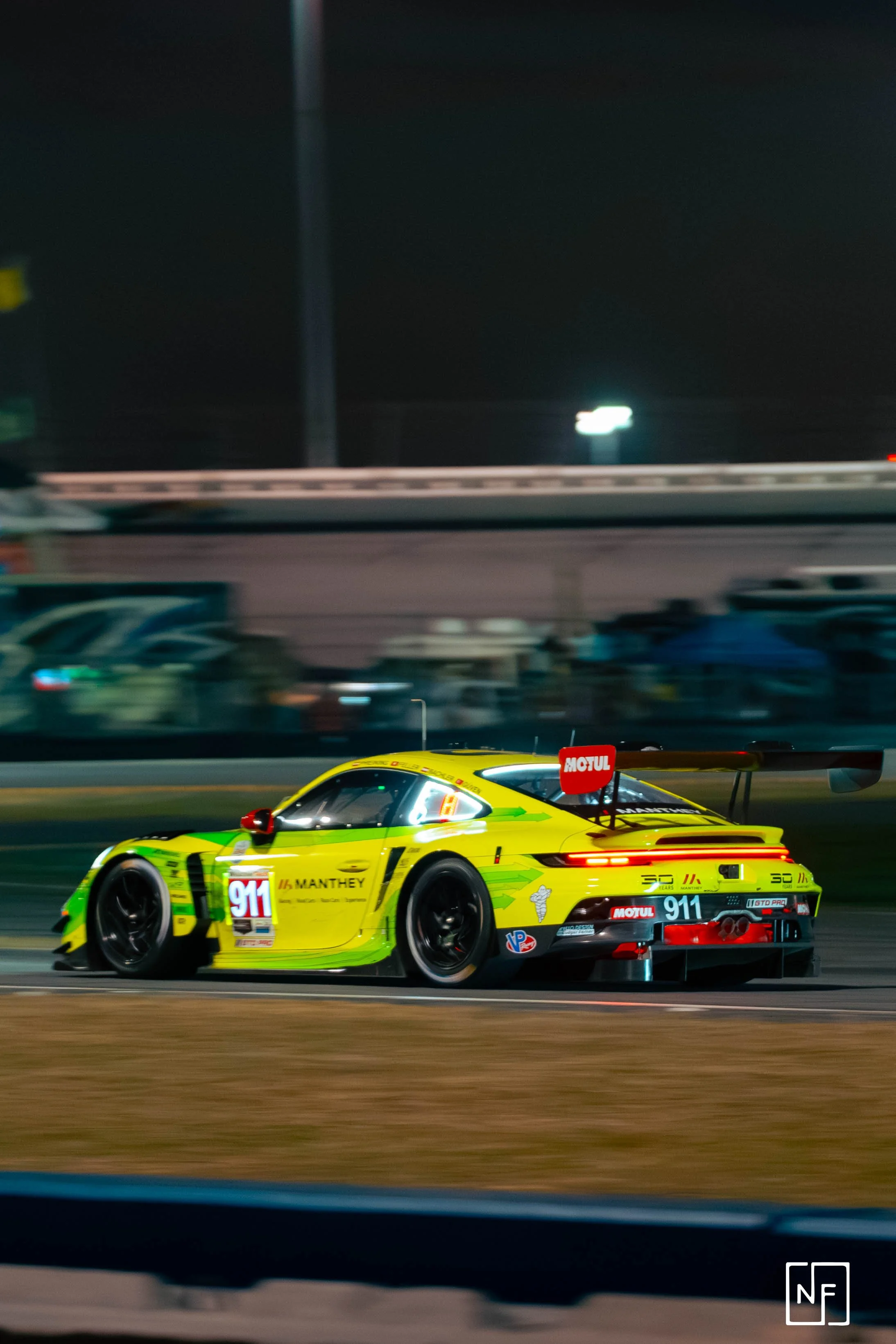 A yellow race car, number 911, driving on a race track at night, with blurred background and tire smoke.