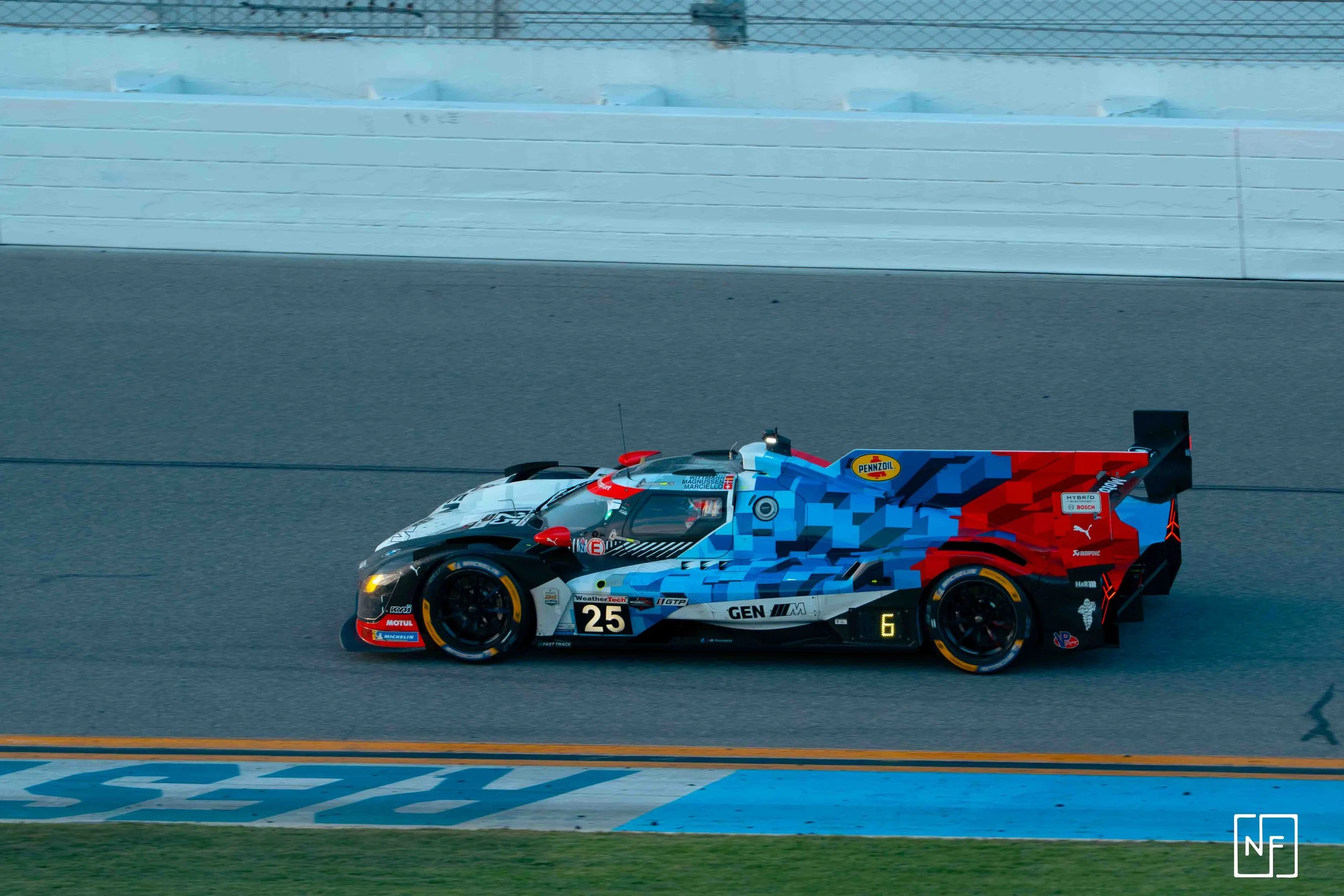 Race car on track with pixelated blue and red design, yellow wheels, and various sponsor logos.