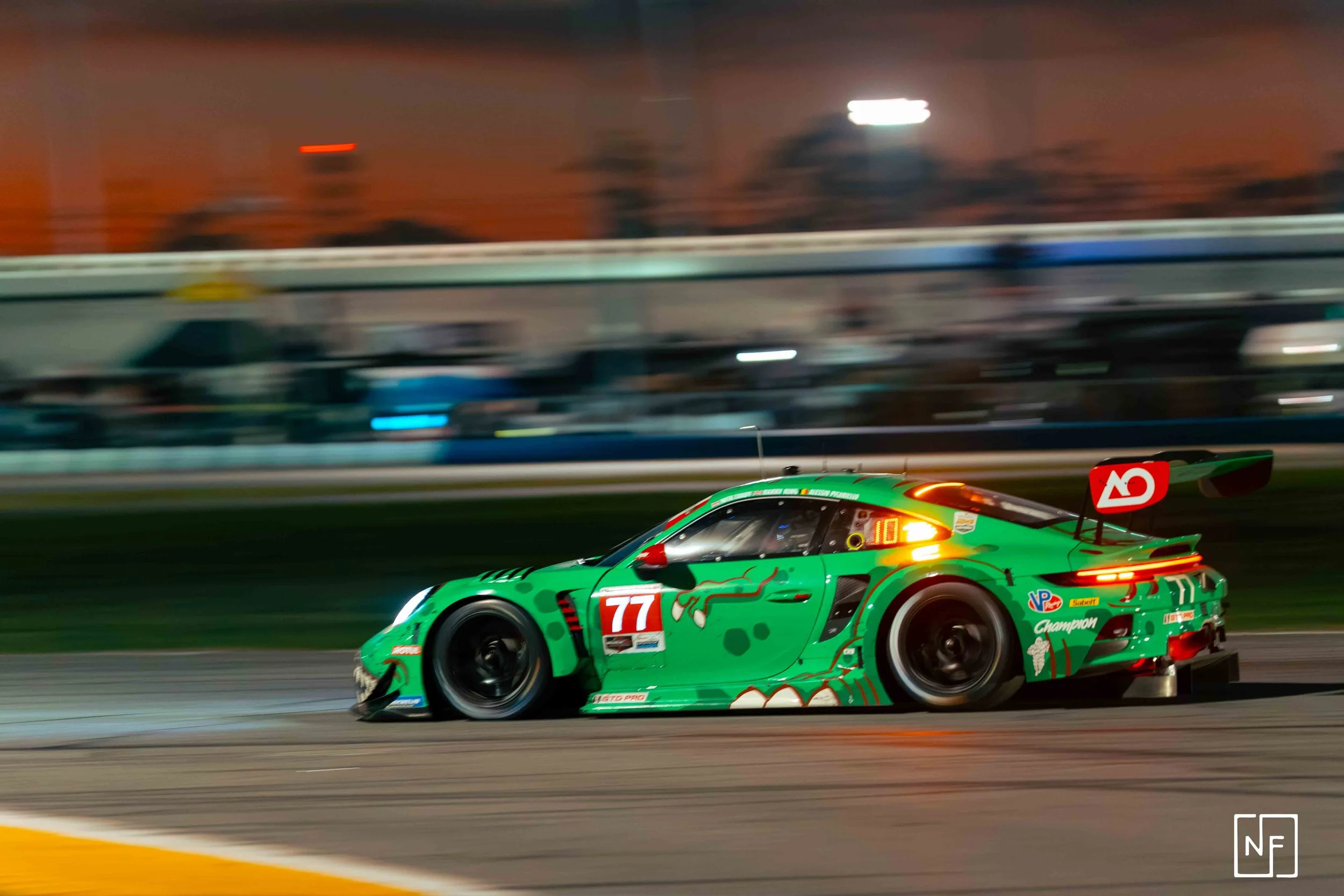A green race car speeding on a track at dusk with a blurred background.