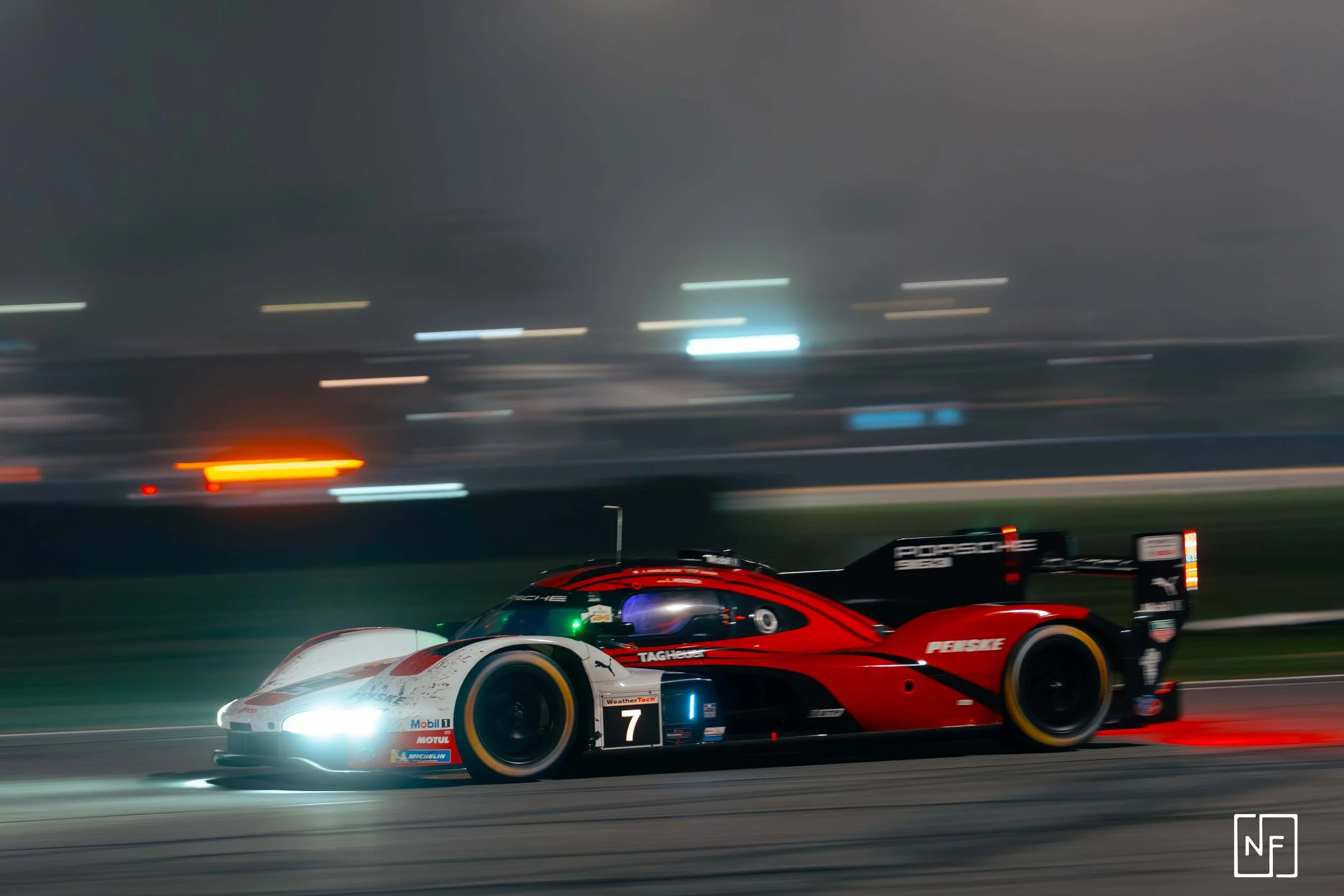 A sports car racing at night on a track, with headlights on and blurred lights in the background.